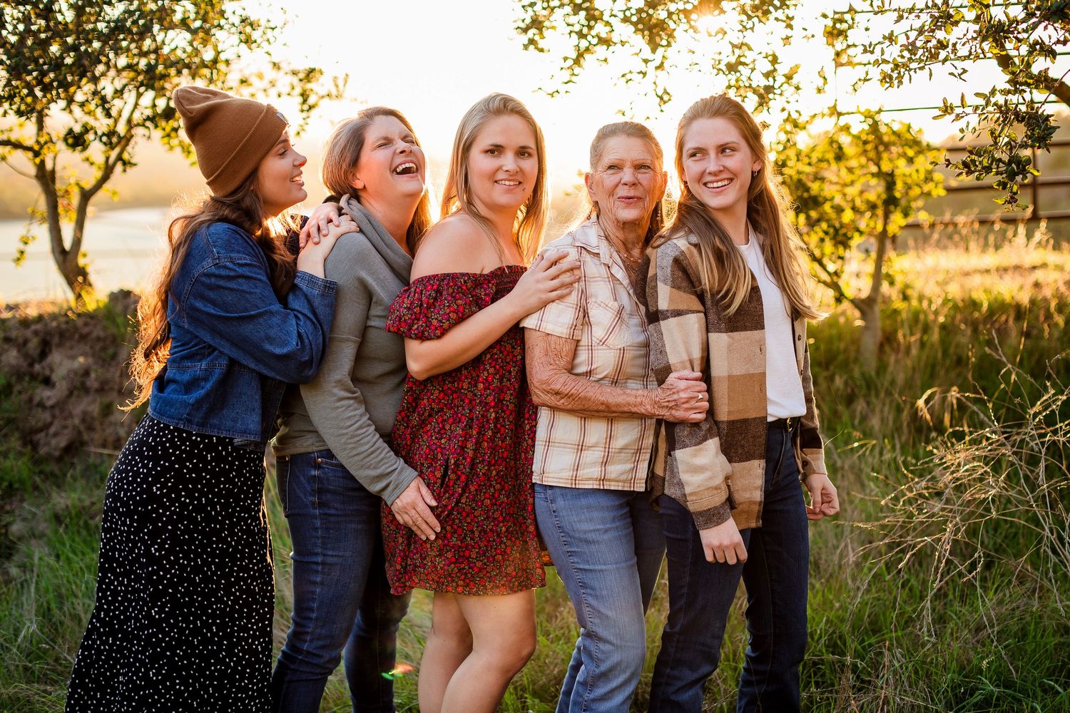 Group of friends laughing together outdoors during golden hour sunset in a grassy field.