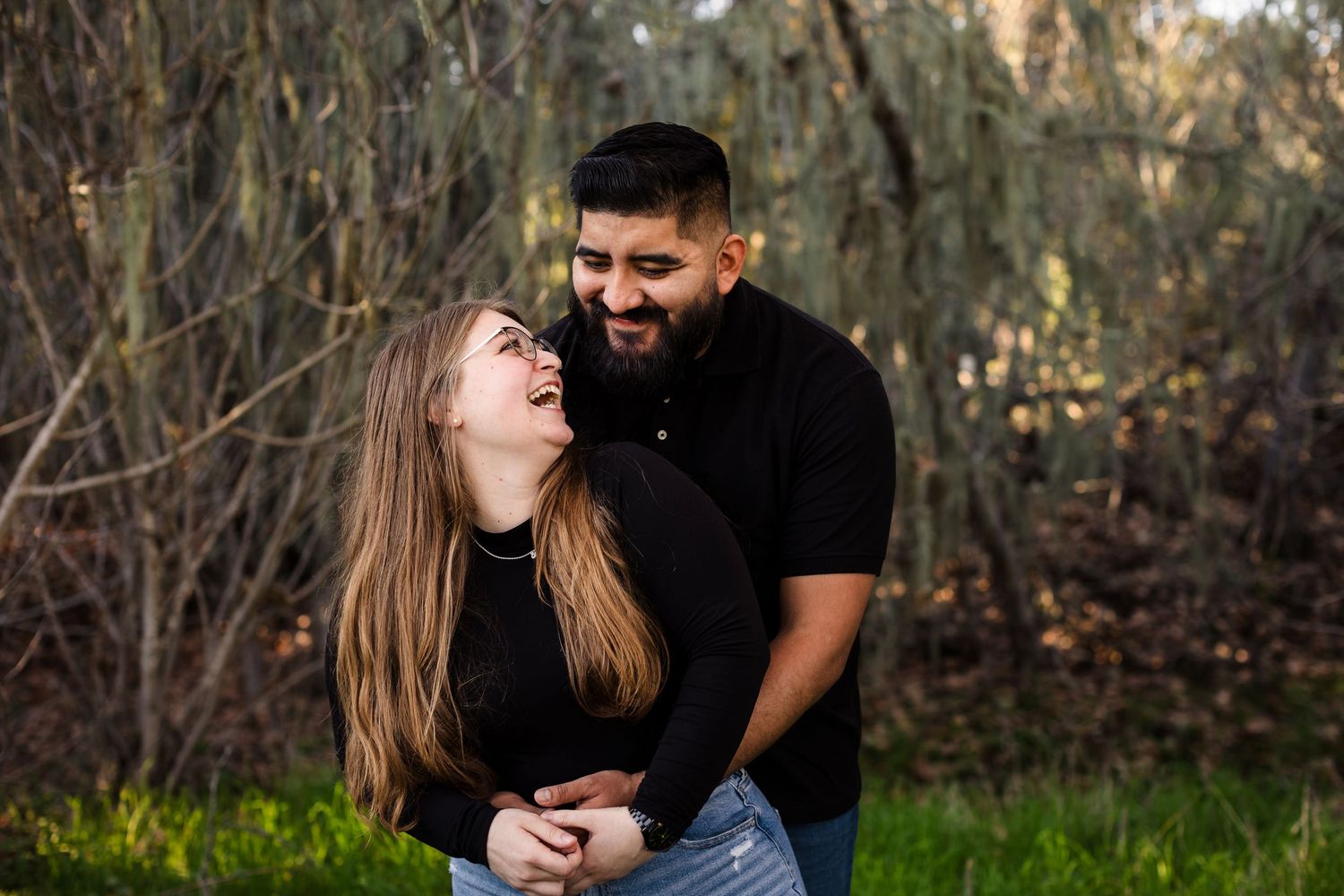 A couple shares intimate moments in an outdoor photoshoot against a natural wooded backdrop during golden hour.