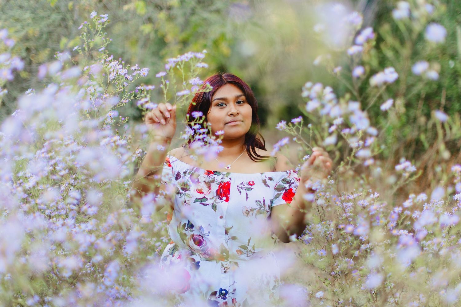 Someone wearing a floral dress poses dreamily in a meadow of delicate white wildflowers on a soft summer day.