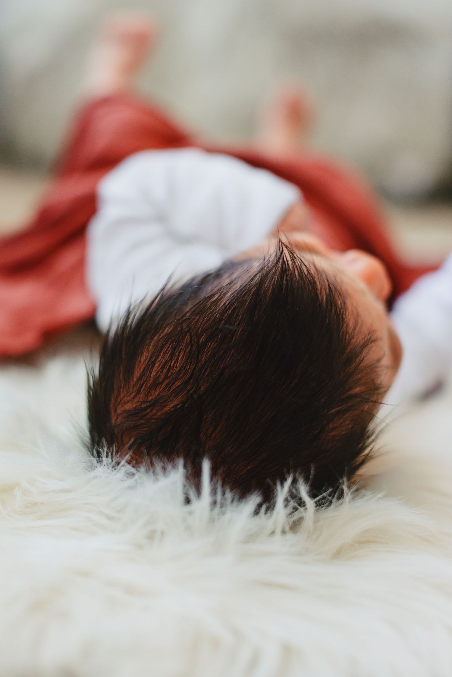 Close-up view of dark hair against soft white fur blanket with red clothing visible.