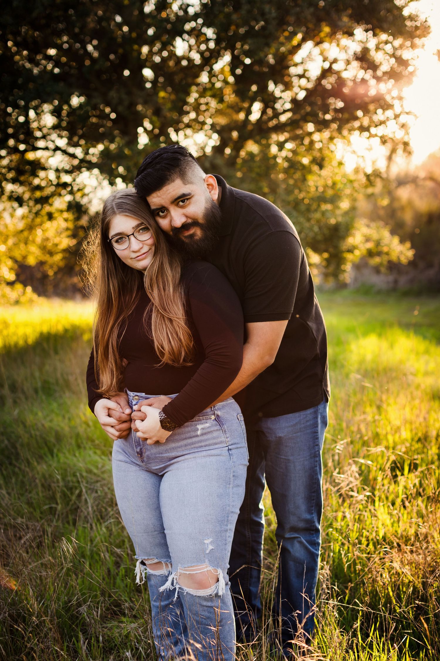 A couple shares tender moments in a sunlit meadow during golden hour while embracing and laughing together.