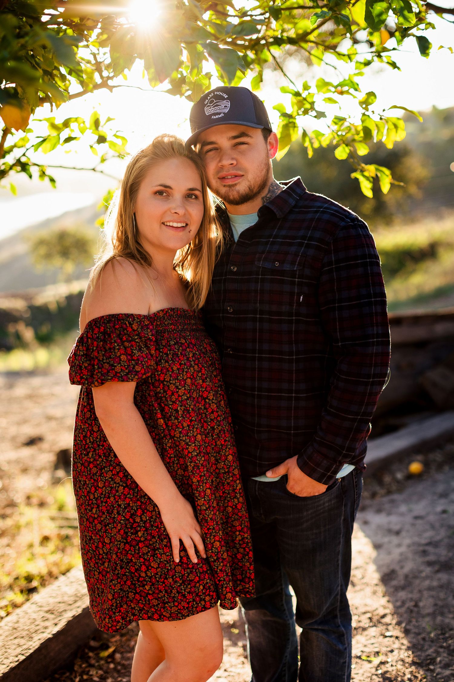 Couple poses together for romantic sunset engagement photos in nature with sunlit trees and foliage in the background.