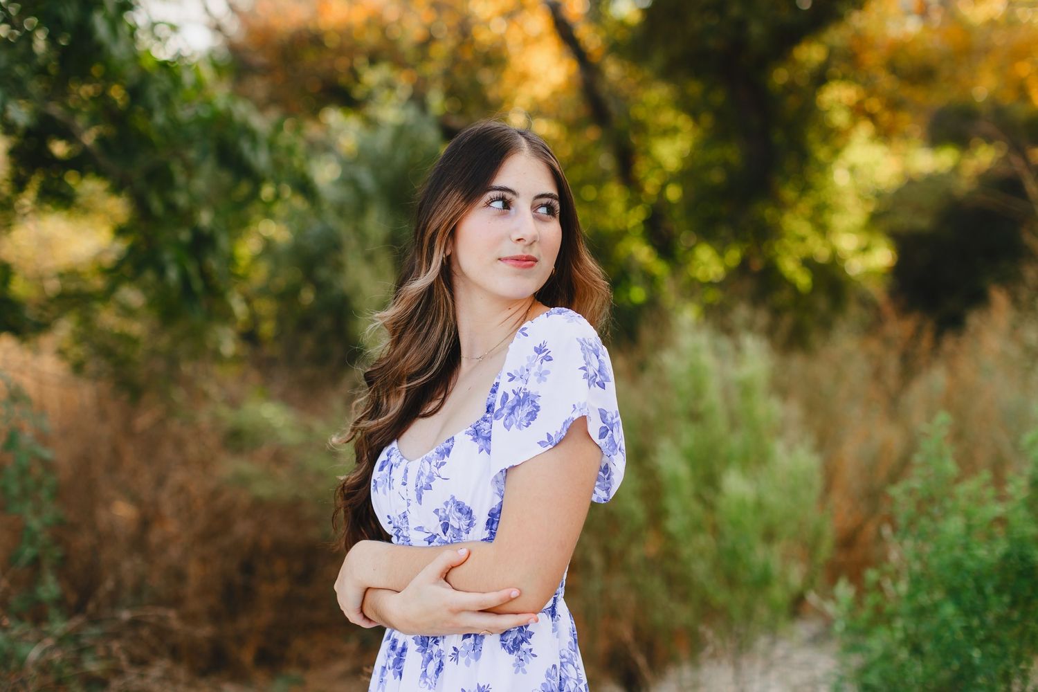 A woman in a floral white dress walks through a beautiful autumn field at sunset.