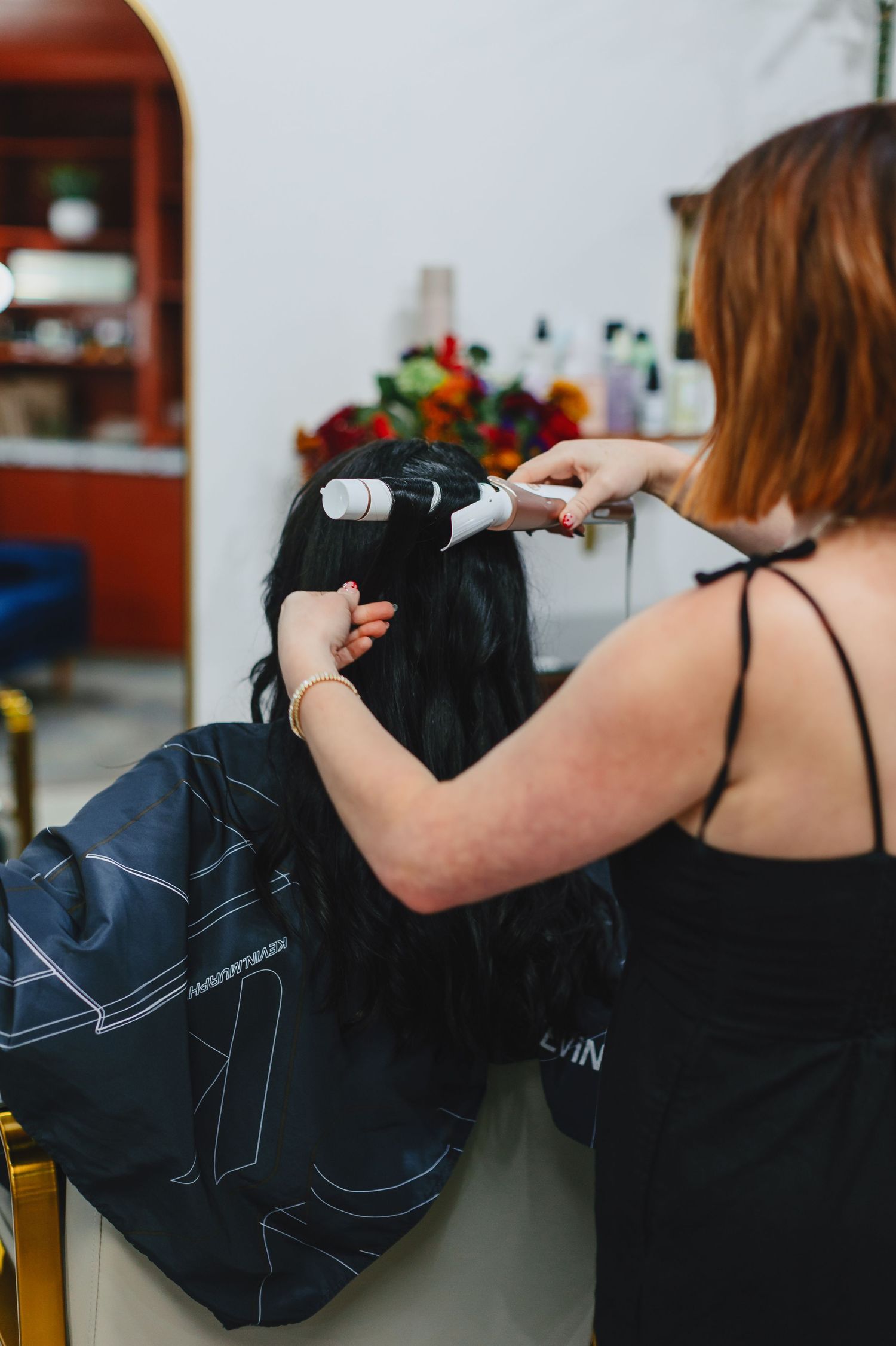 Stylist using hair dryer and brush on client in salon chair.