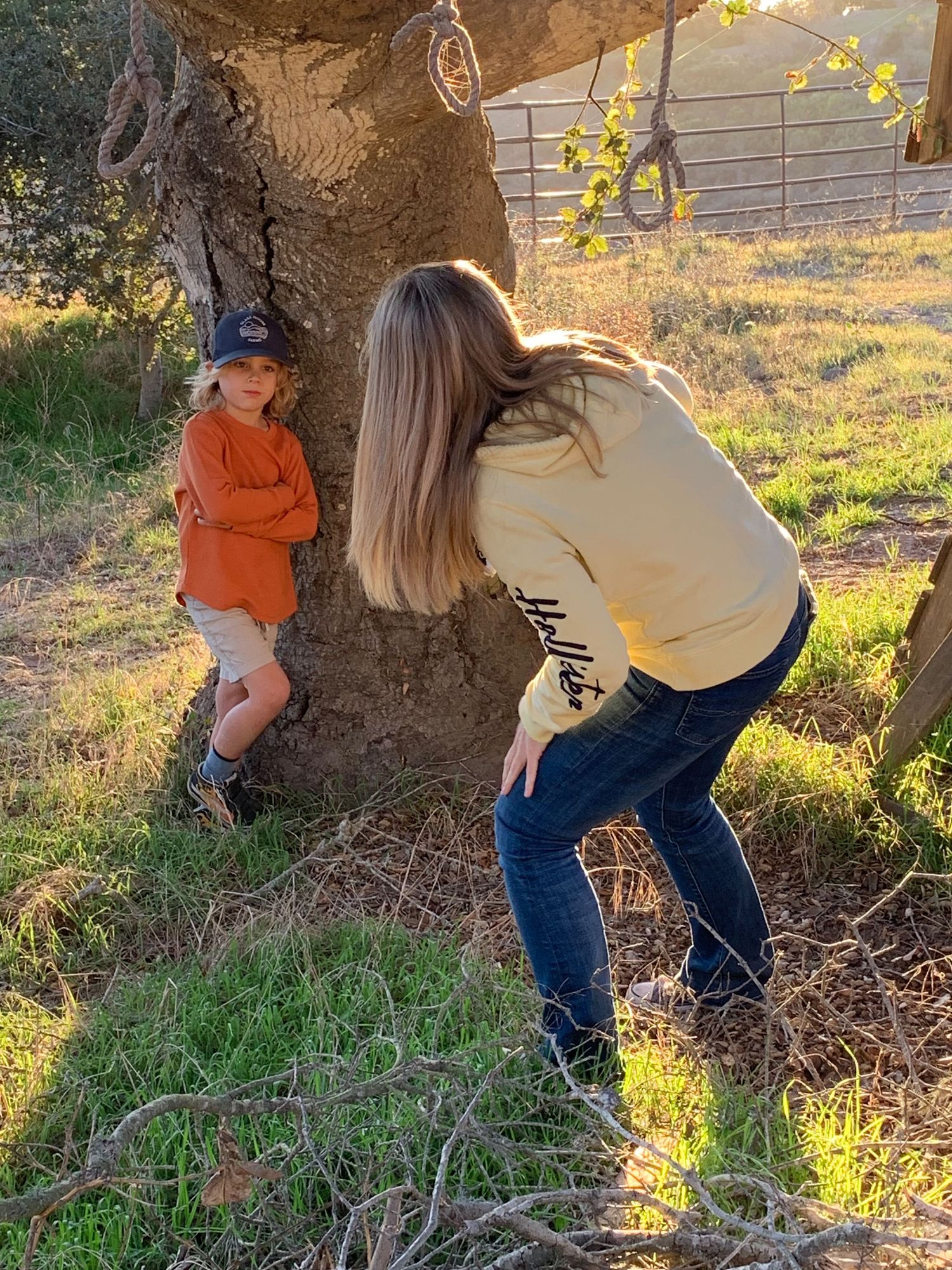 Photographer crouching to photograph a young child leaning against a large oak tree outdoors.