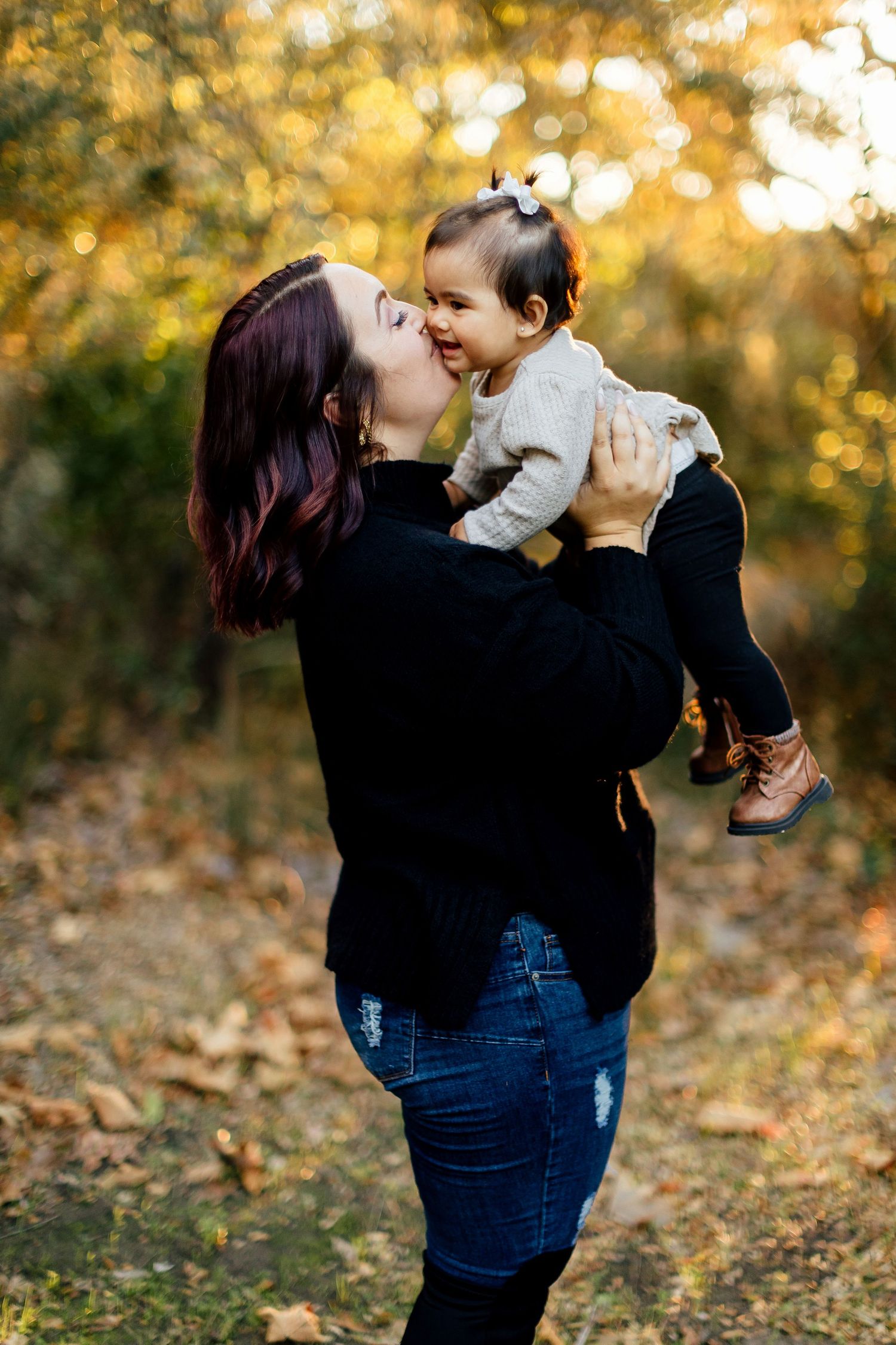 Parent and child share tender moments in autumn forest setting with golden sunlight filtering through trees.