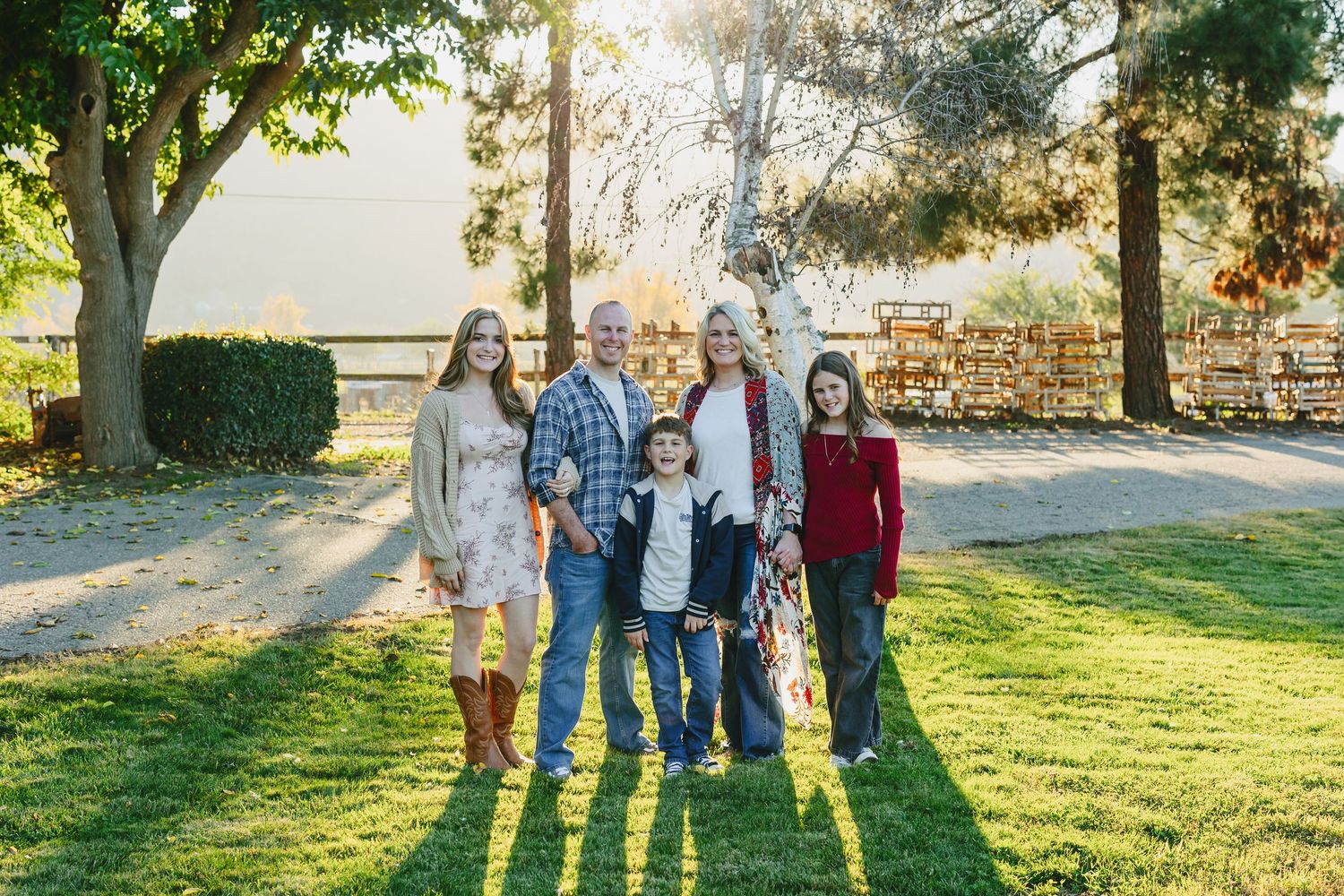 A group stands together on a sunlit grassy lawn during golden hour casting long shadows behind them.