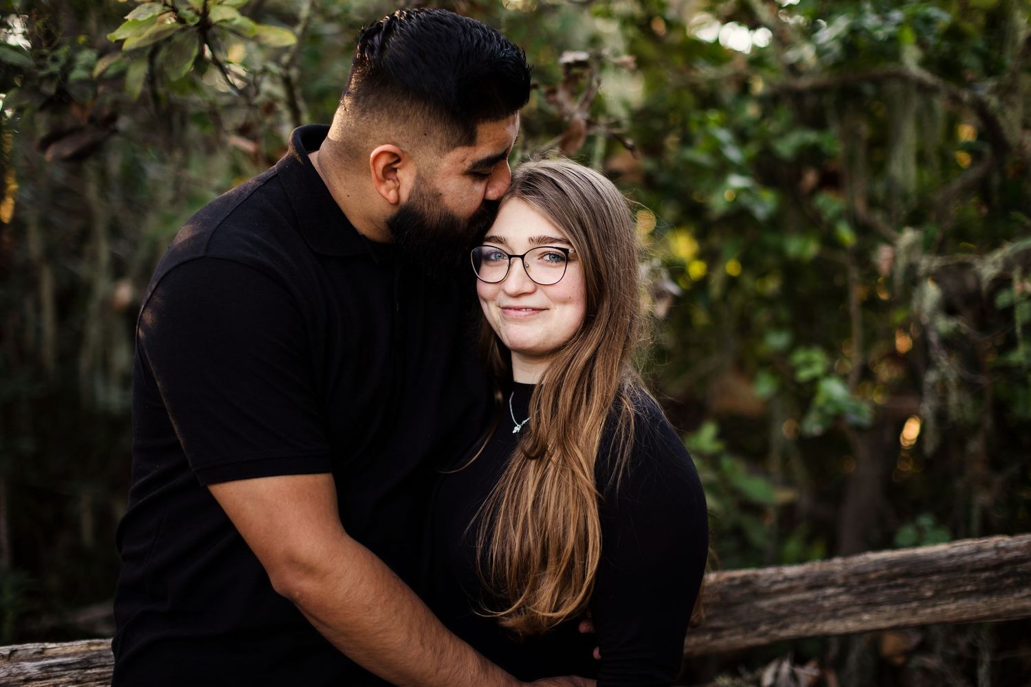 A romantic couple embraces against natural greenery during a photo session in a forest setting.