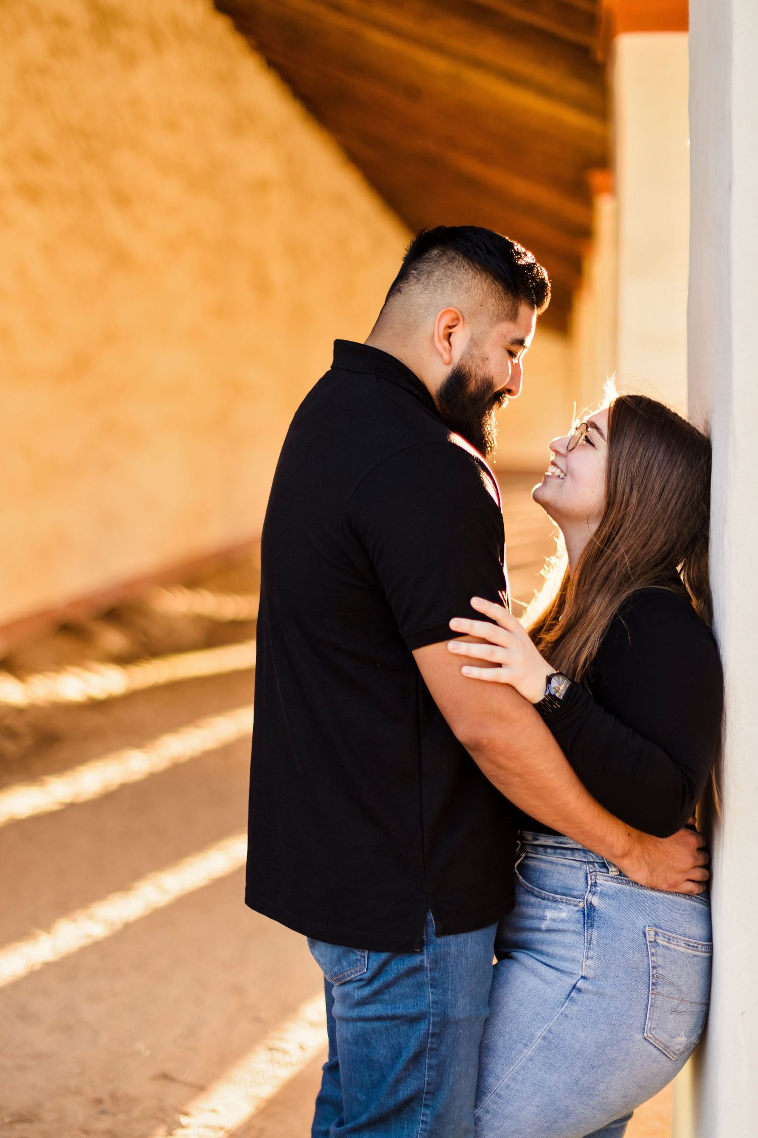 A romantic couple in casual attire sharing an intimate moment against an orange-tinted concrete structure.