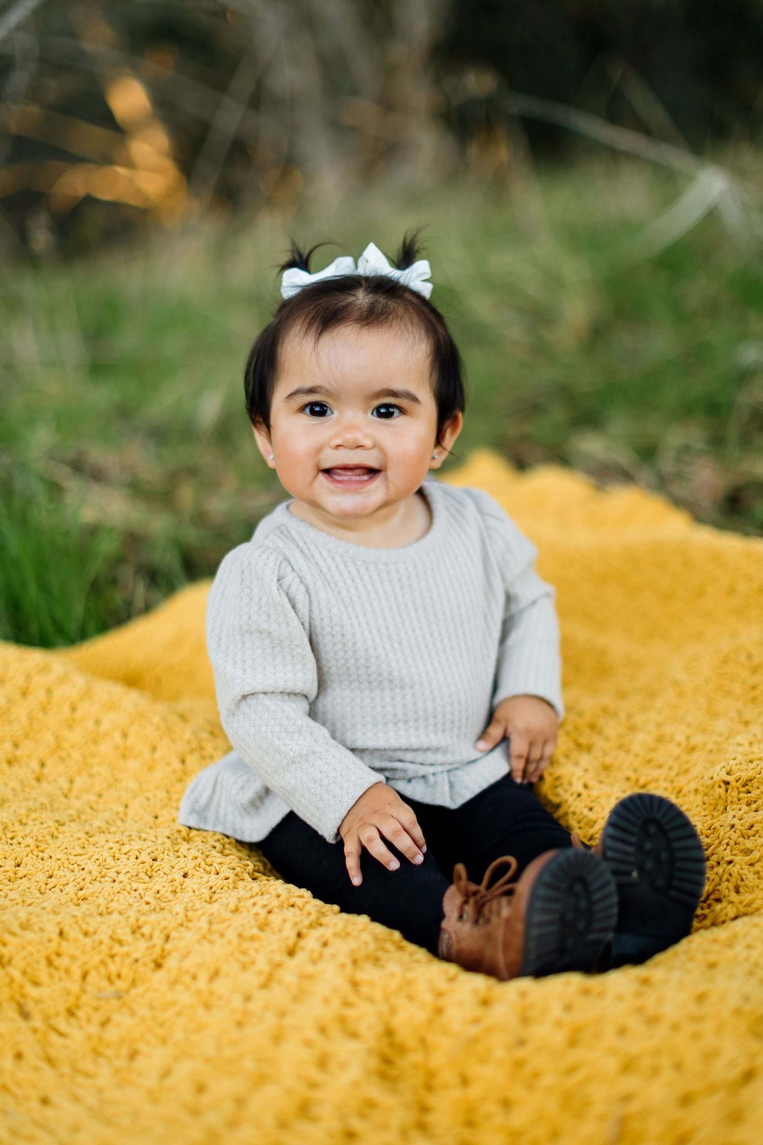 Child wearing a light gray sweater sits on a bright yellow textured surface with a joyful expression.