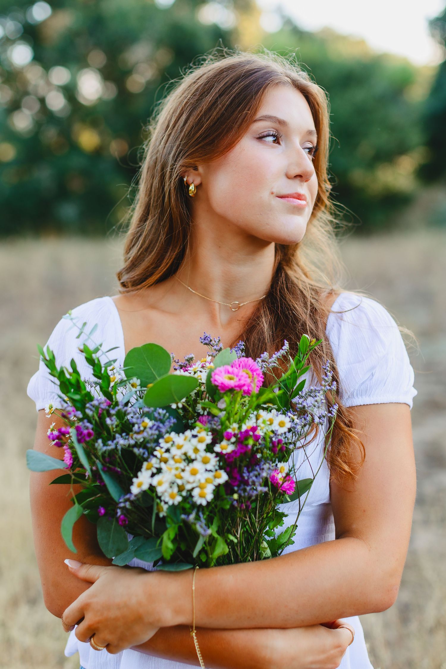 Woman in white dress holds colorful wildflower bouquet in summer field.