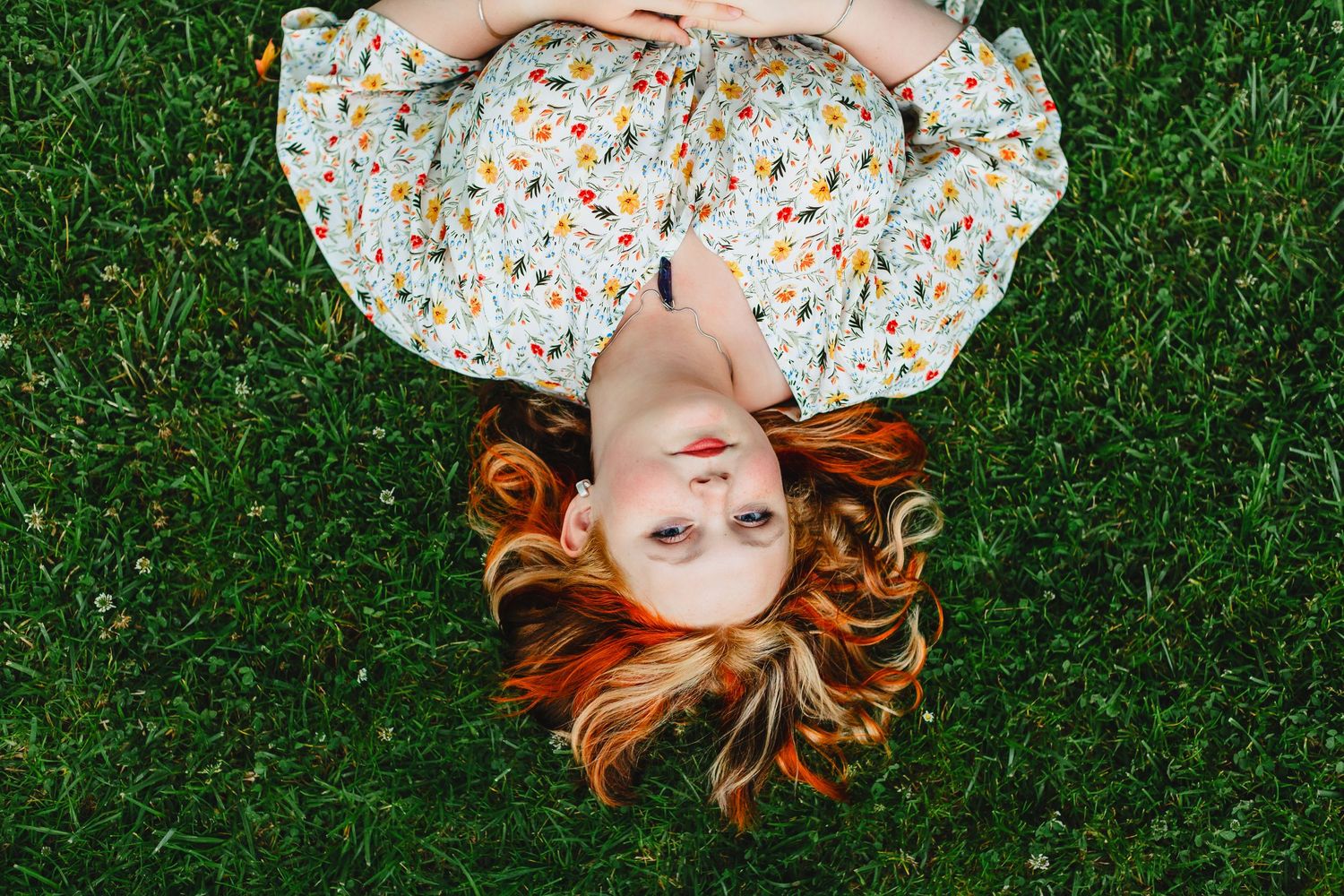 A person with red hair lies on green grass in seven sequential photos creating a circular pattern.
