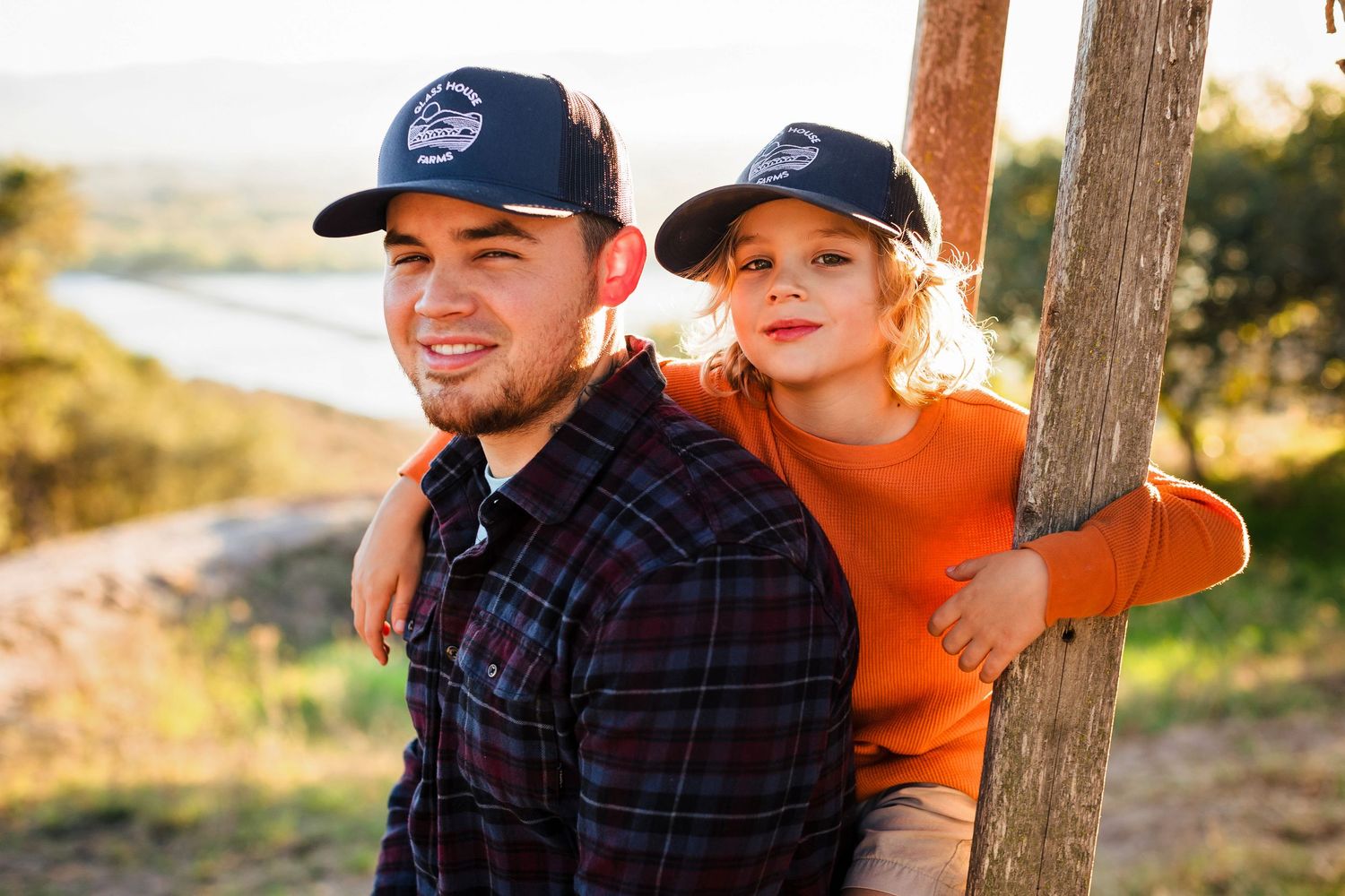 Couple sharing a tender moment on a sunny path while wearing casual outdoor clothing and baseball caps.