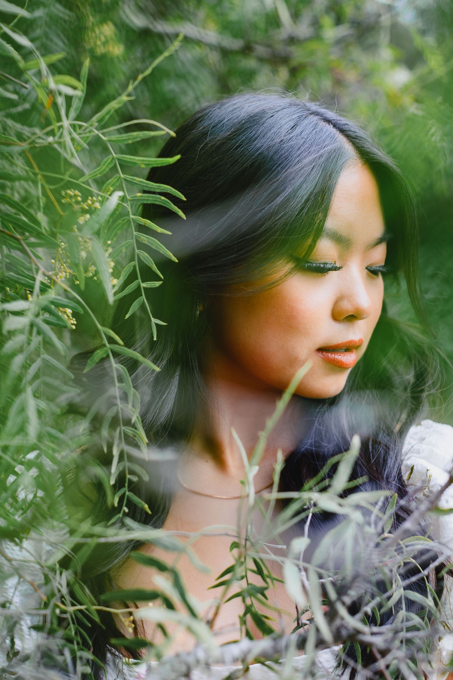 Artistic portrait of woman surrounded by delicate foliage in natural lighting.