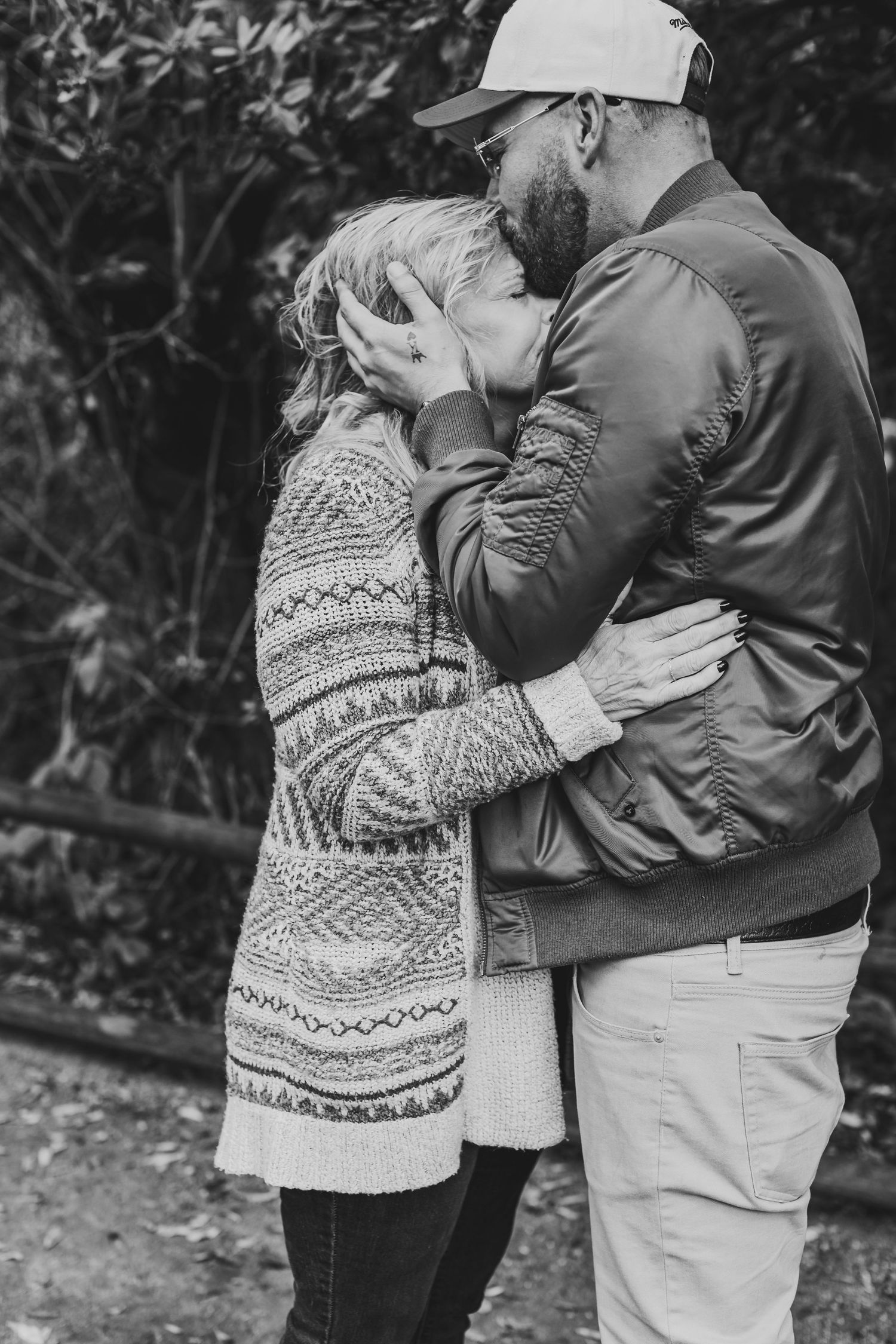 Black and white photo of couple in warm sweaters embracing in a garden.