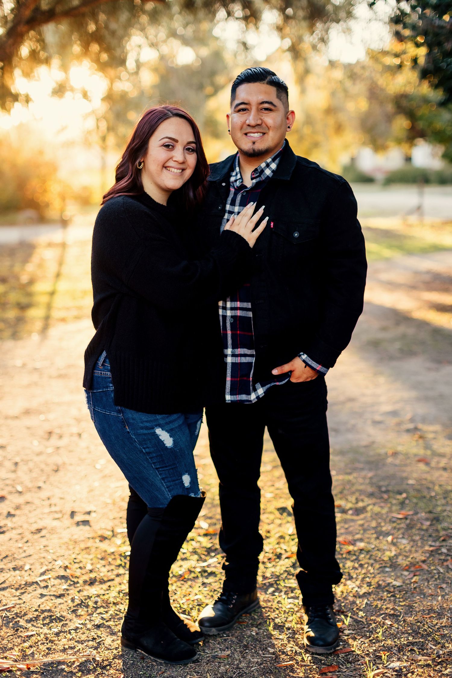 A couple poses outdoors during golden hour sunset, sharing intimate moments in a park setting with autumn lighting.