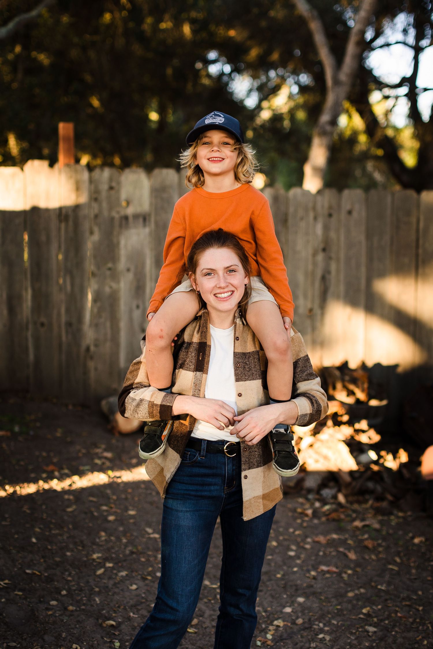 Two people playing outdoors share a joyful moment in front of a wooden fence during golden hour.