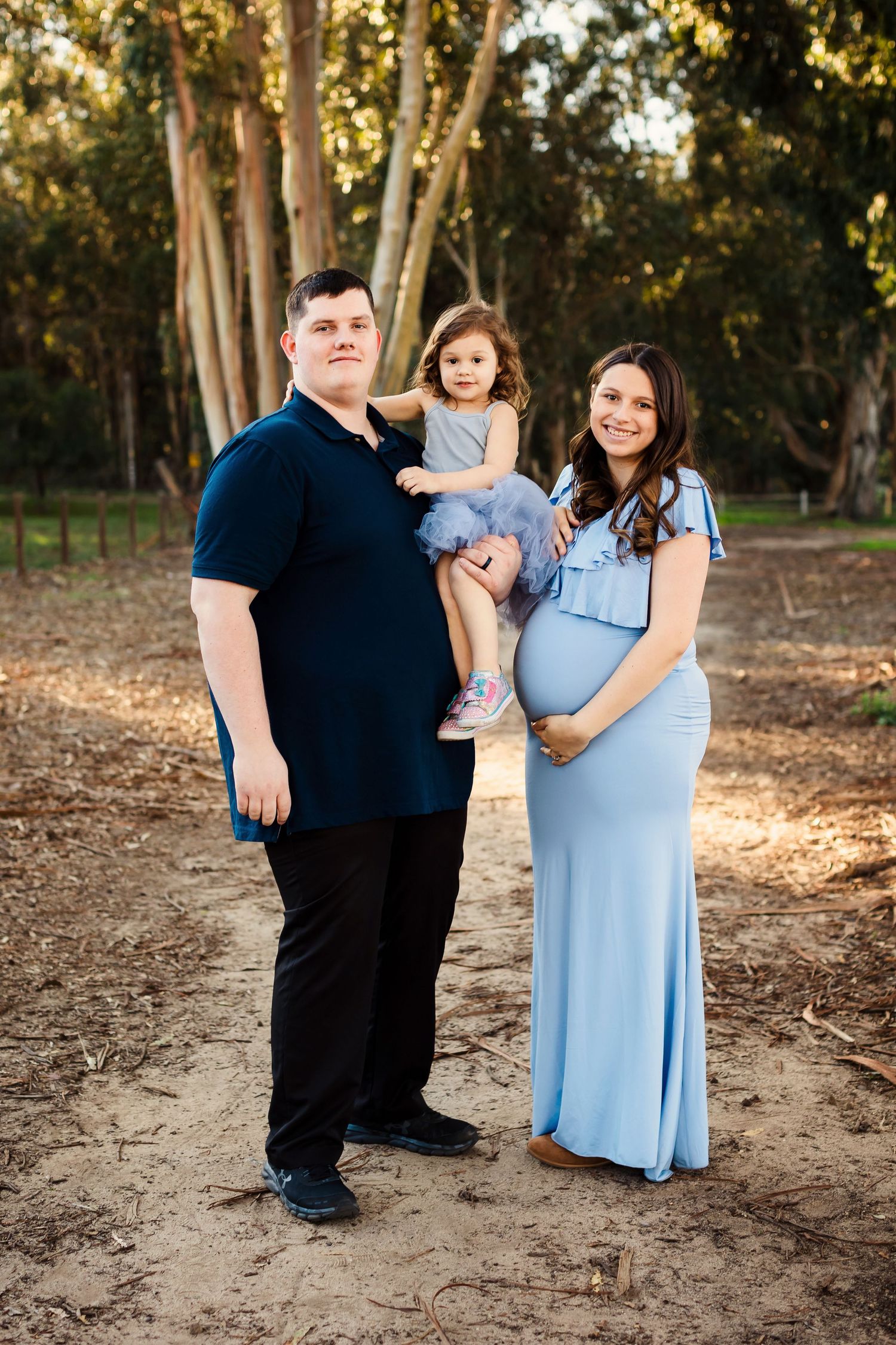 A family poses together outdoors in a wooded setting during golden hour.