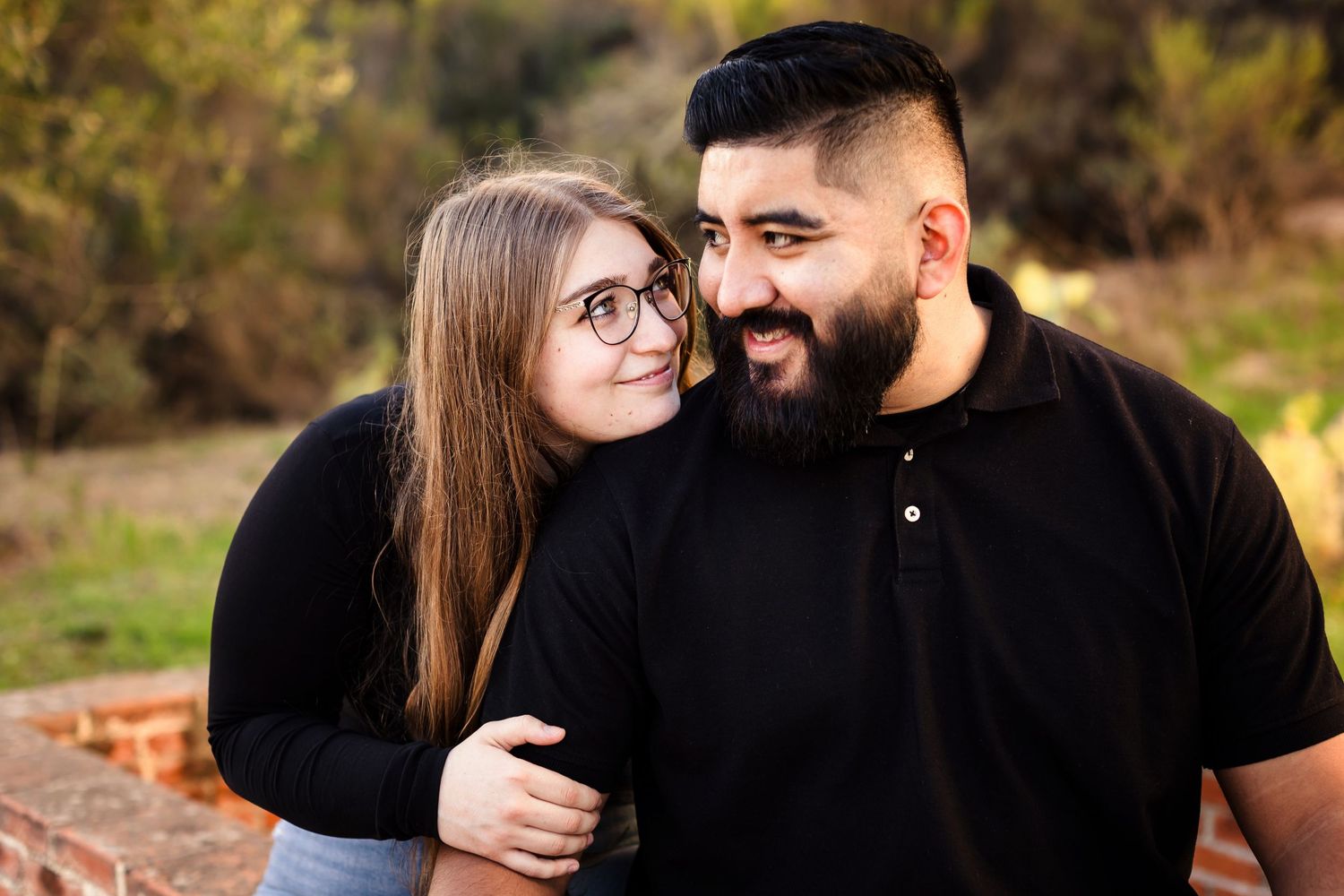 Couple in matching black outfits embrace and share a tender moment outdoors during autumn.