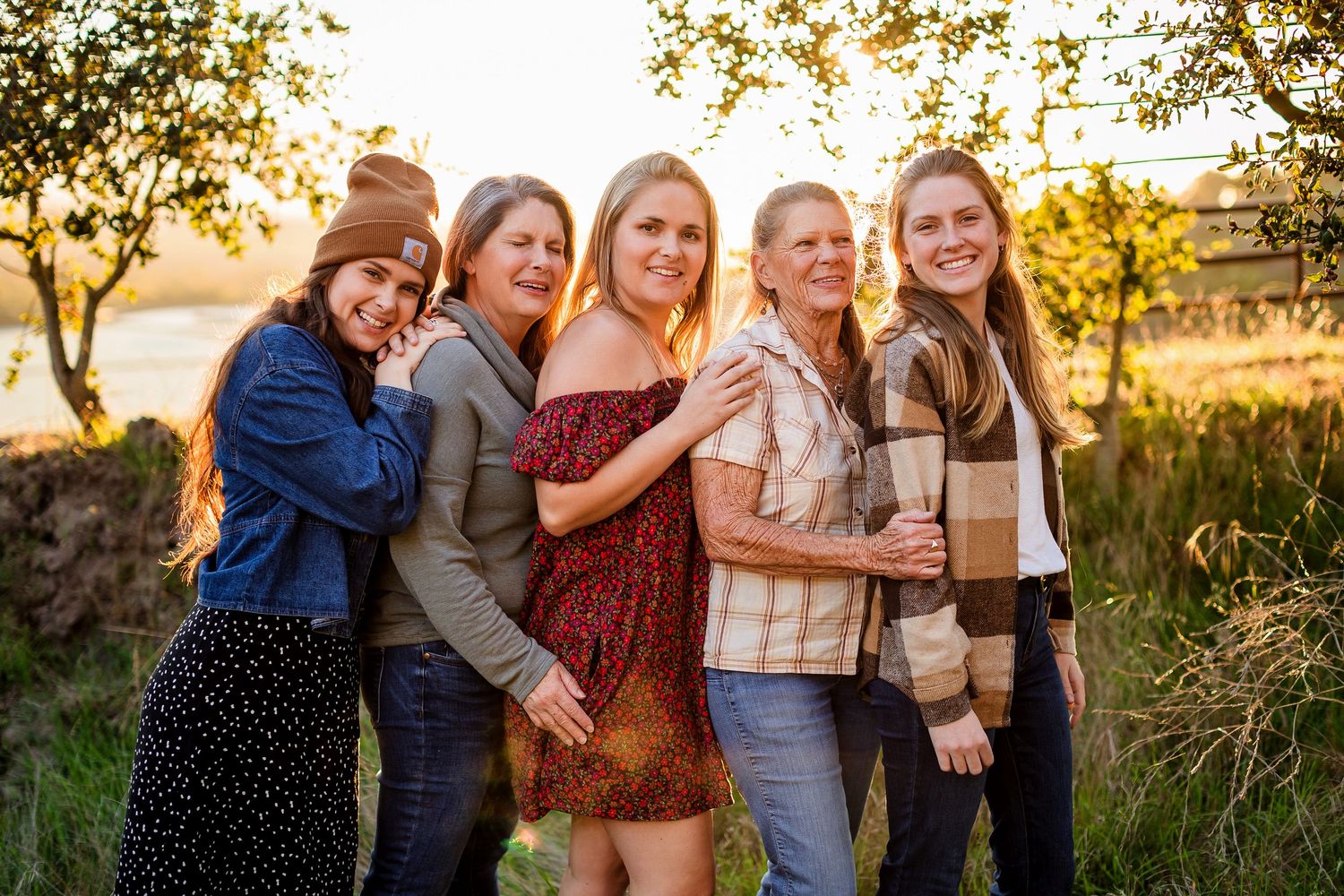 Group of friends laughing and embracing together during golden hour sunset in an outdoor setting.