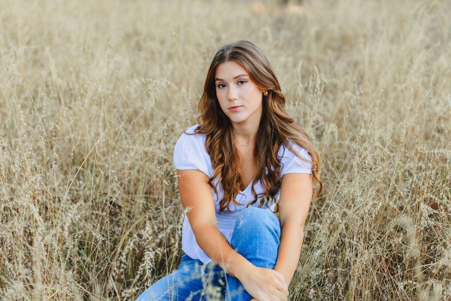 A casual portrait in a golden field features a contemplative pose and white top with jeans.