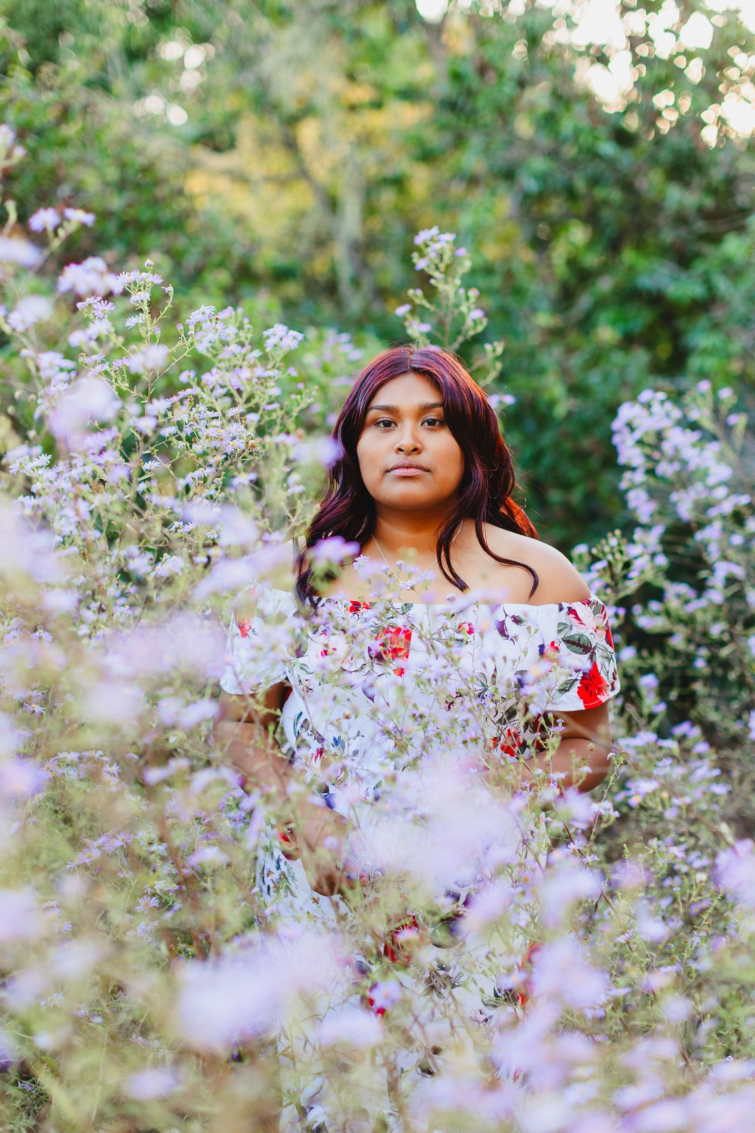 Portrait in blooming garden with purple flowers and off-shoulder floral dress.