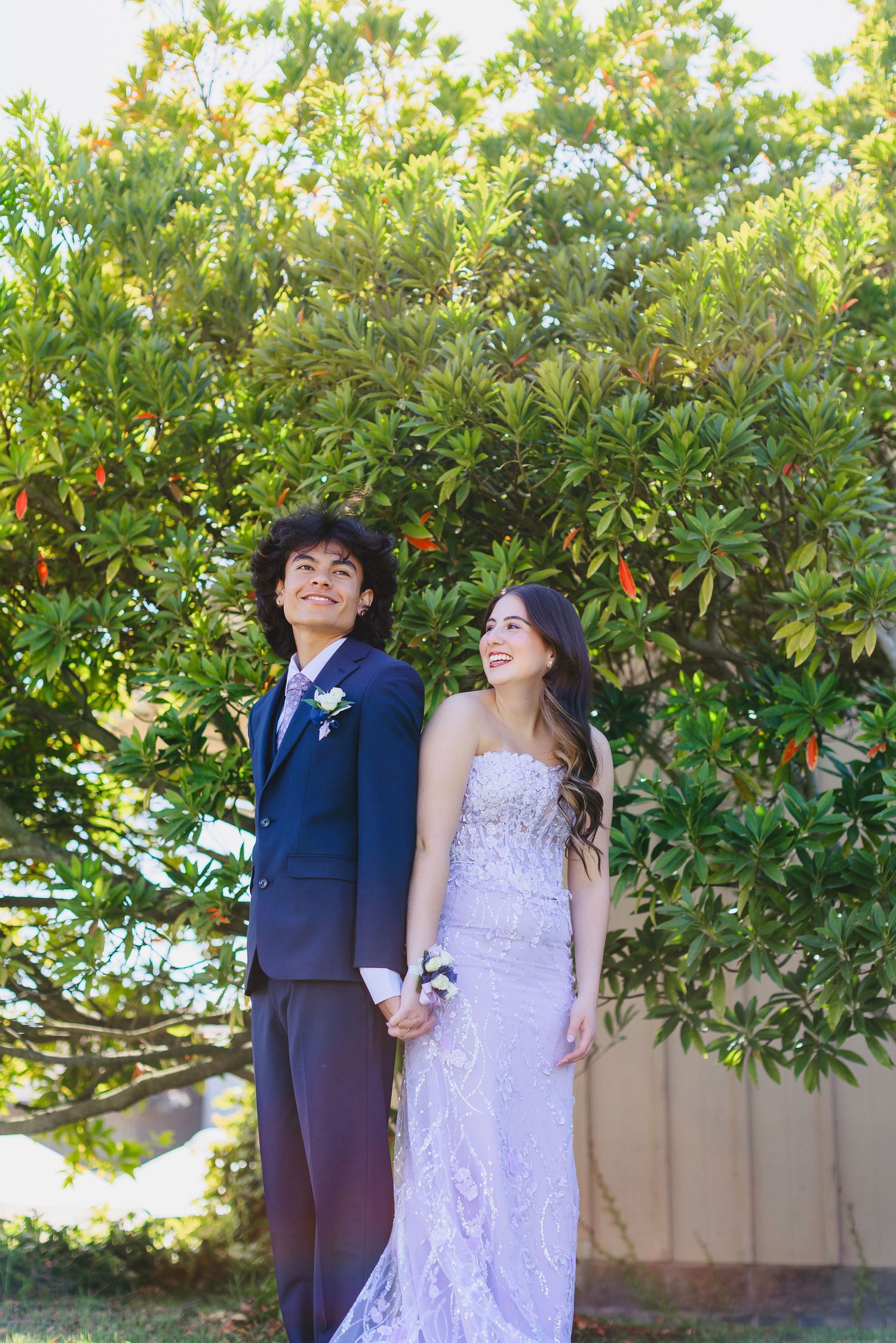 A couple poses against a lush green tree backdrop for formal photos.