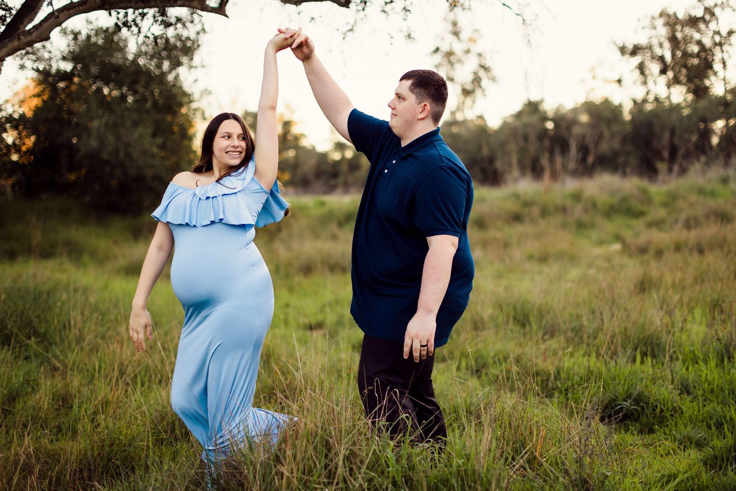 Two people spin together playfully in a grassy field during golden hour.