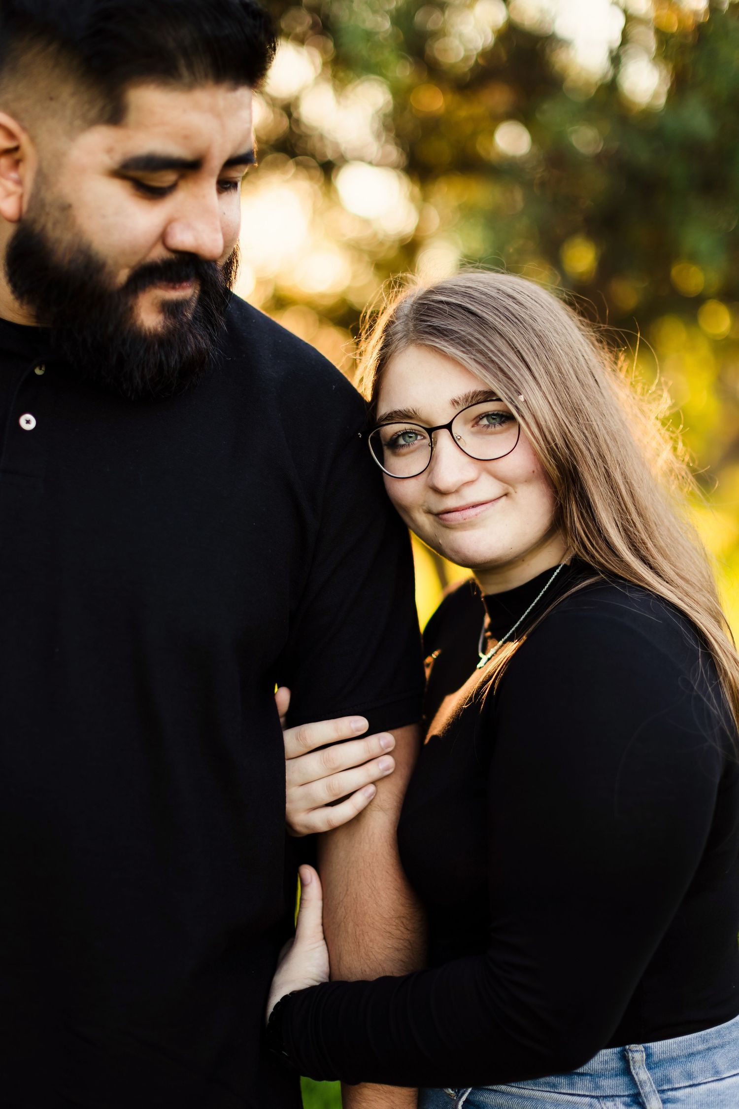 Romantic couple embraces outdoors with golden sunlight filtering through trees in autumn setting.