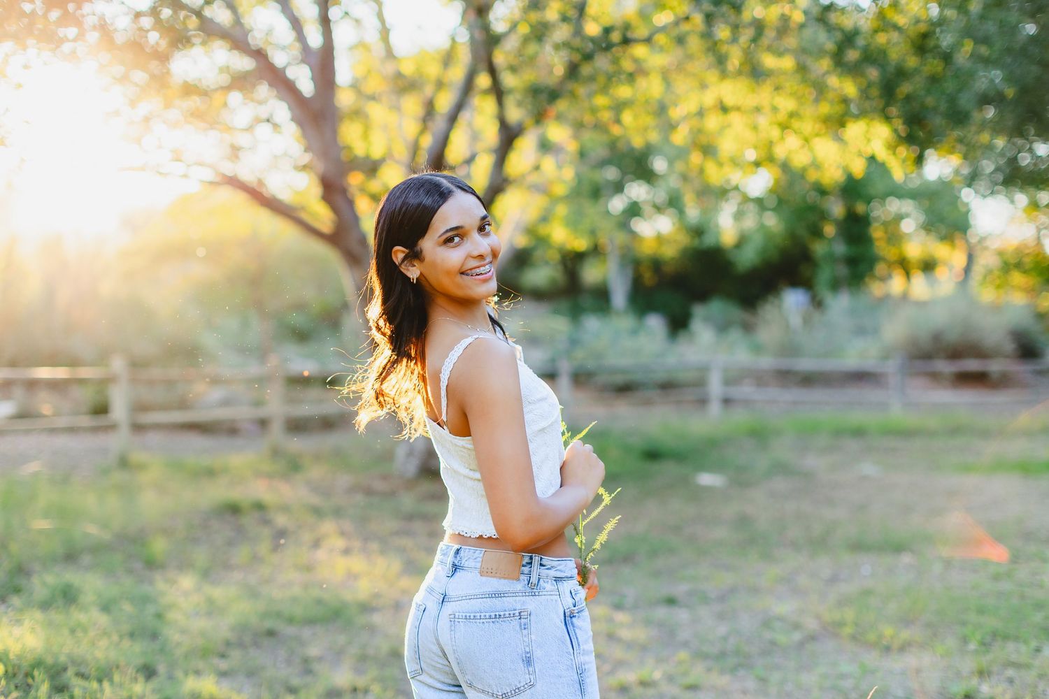 A person in overalls poses playfully in a sunlit garden setting during a golden hour photoshoot.