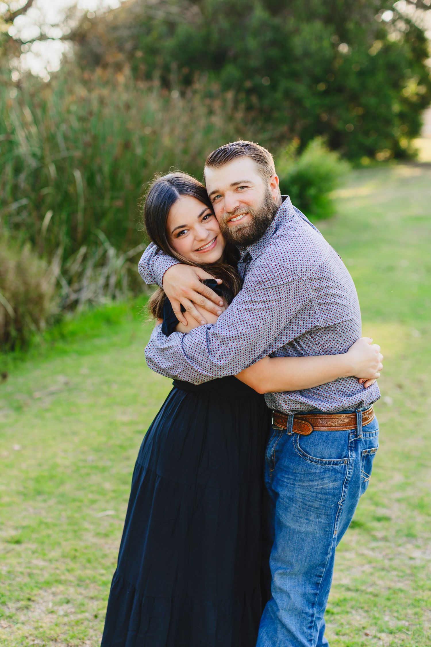 A romantic embrace outdoors with lush greenery in the background.
