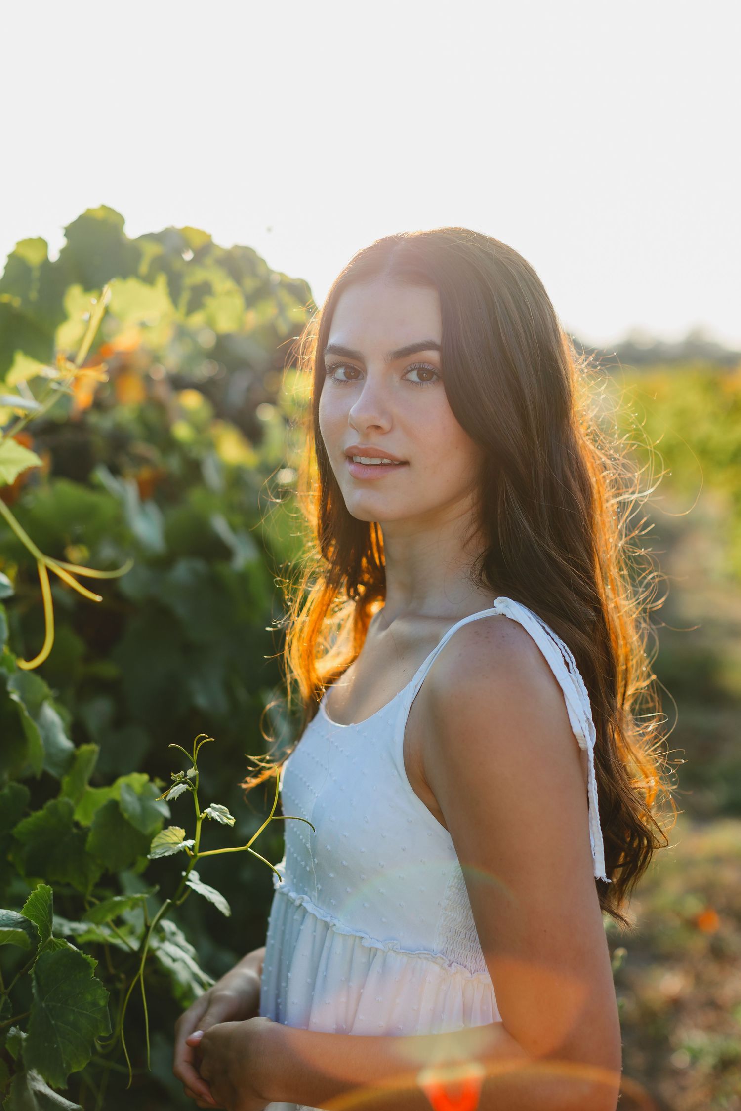 Person in white dress standing in garden with golden sunlight streaming through leaves.