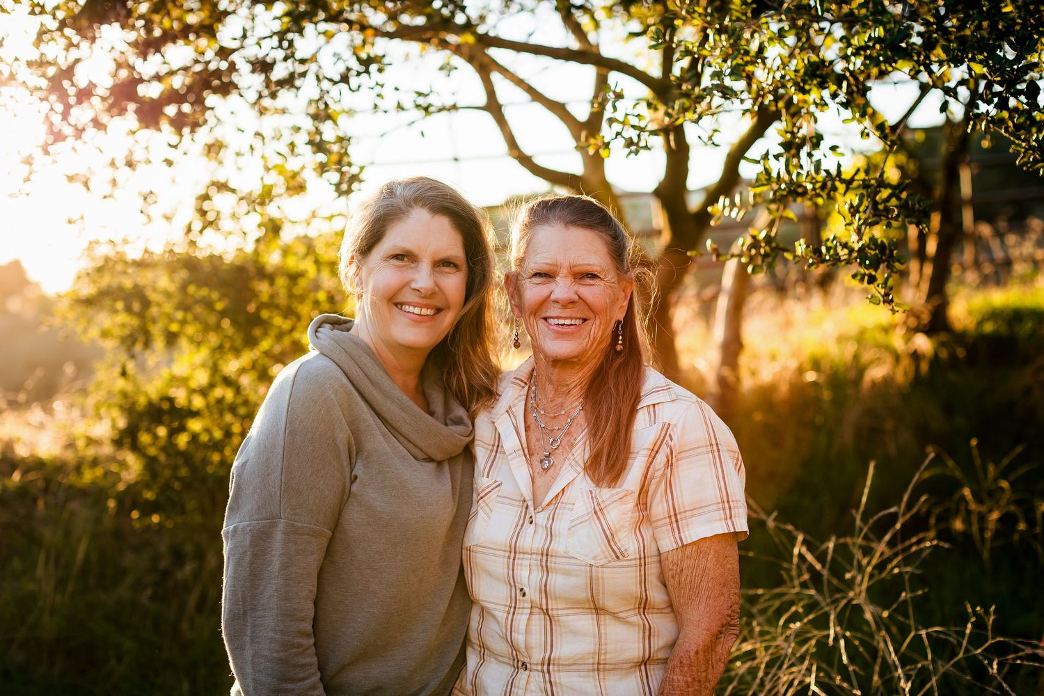 Two people embracing and smiling outdoors during golden hour sunset with trees in background.