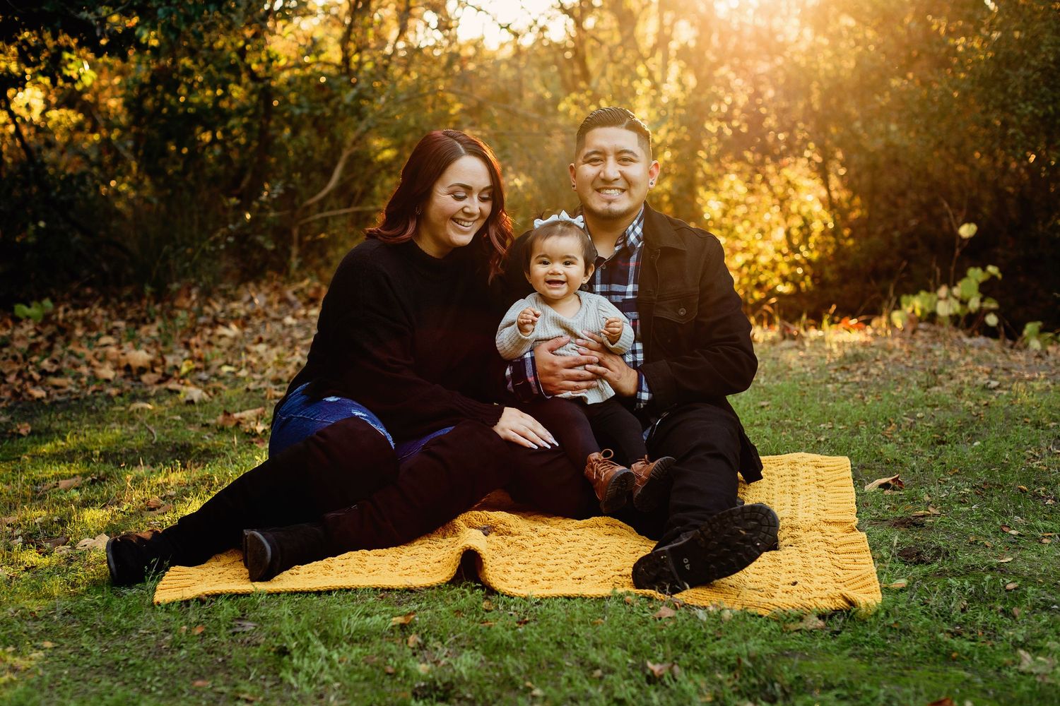 Family sharing warm moments on a yellow blanket in a park during golden hour sunset lighting their joyful expressions.