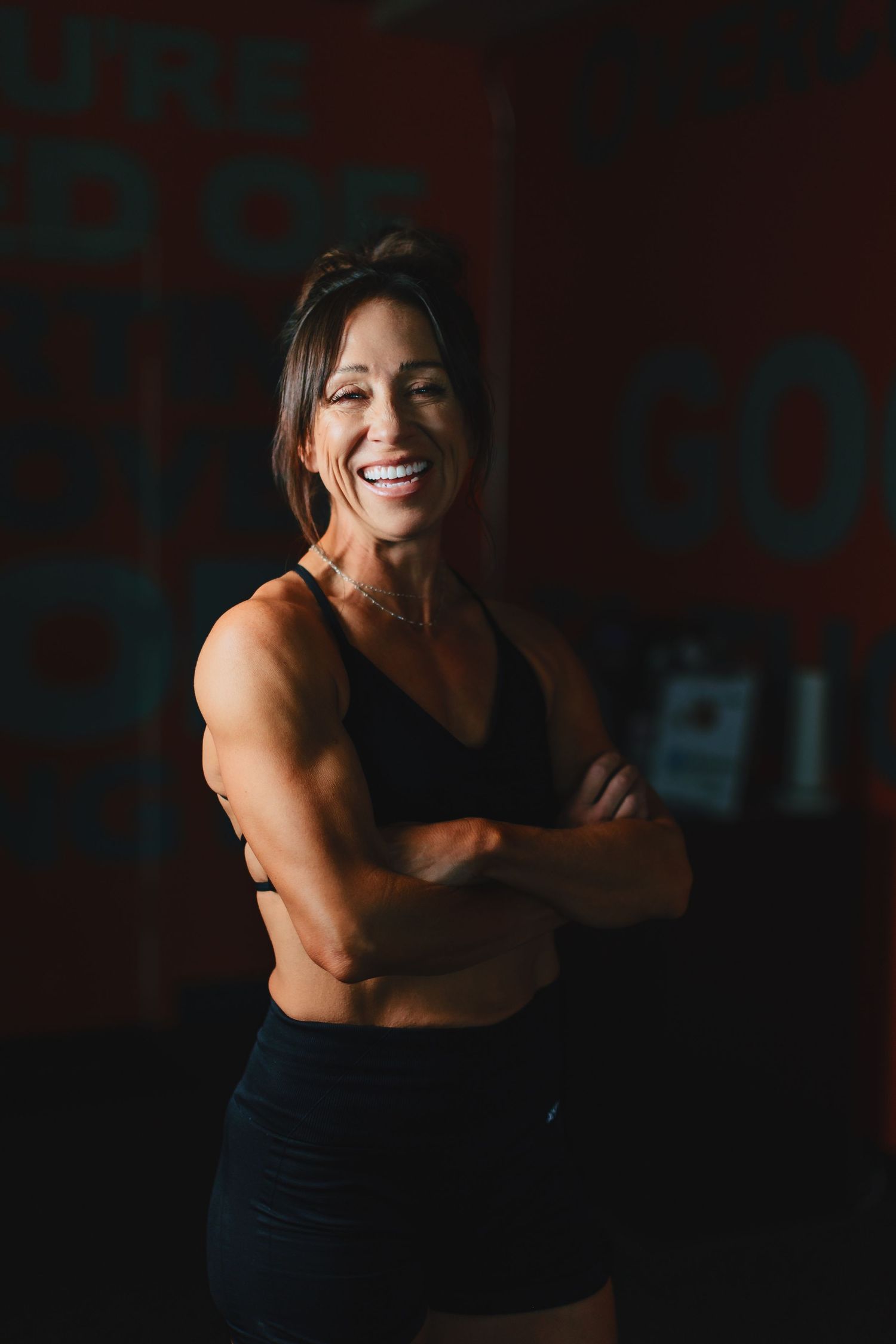 Athletic woman in workout attire smiles confidently in dark gym setting.