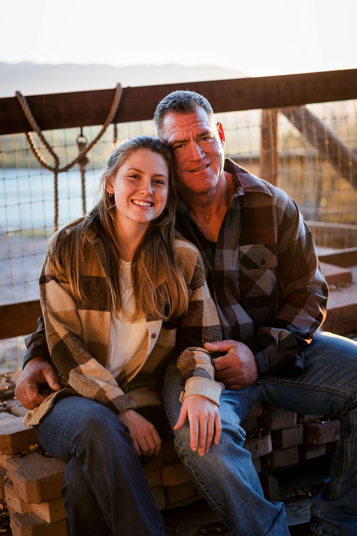 Young couple smiles and shares intimate moments together while sitting on wooden bench in warm sunlit setting.