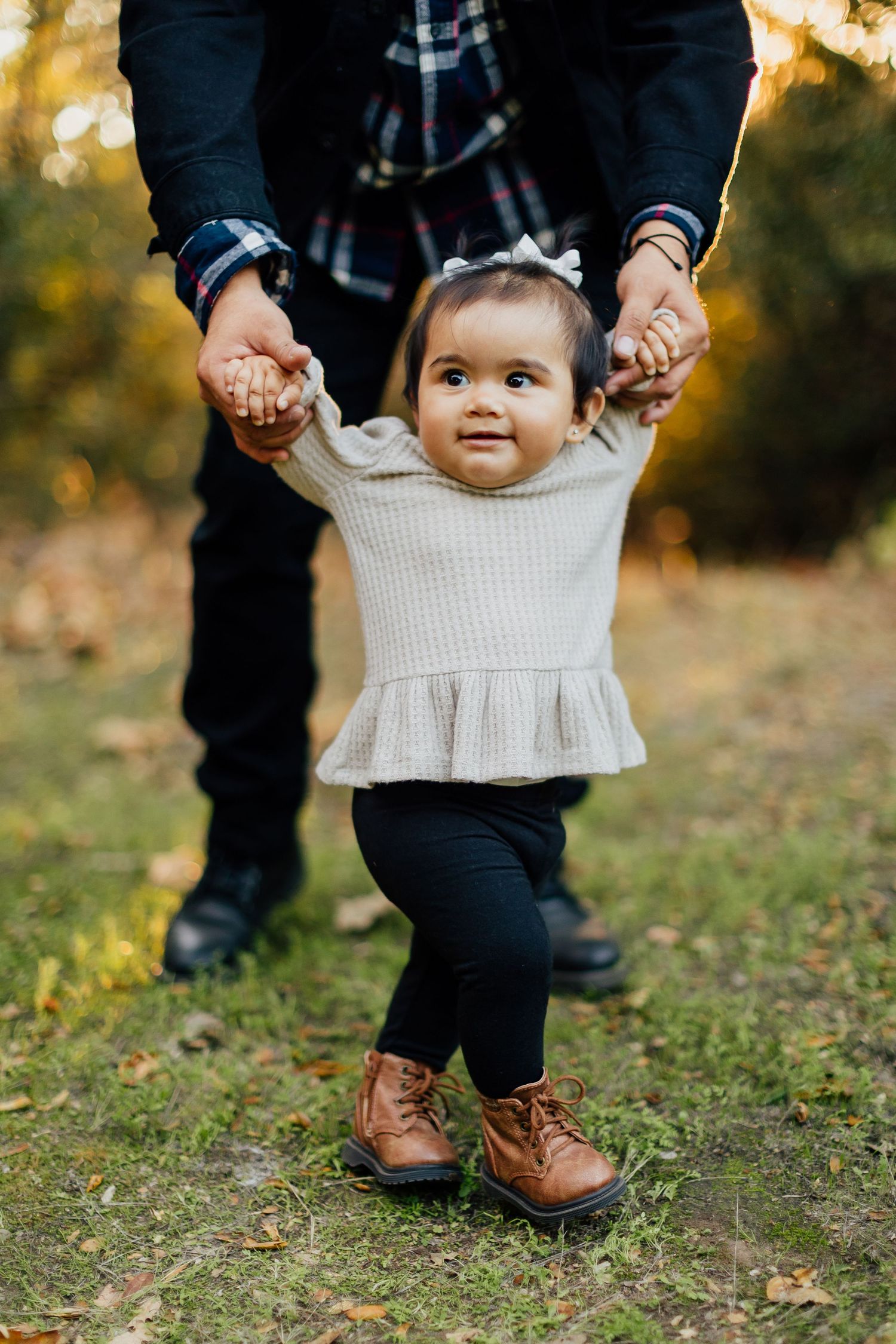 Three cropped photos showing brown leather boots and black pants while holding a small child in a cream sweater outdoors.