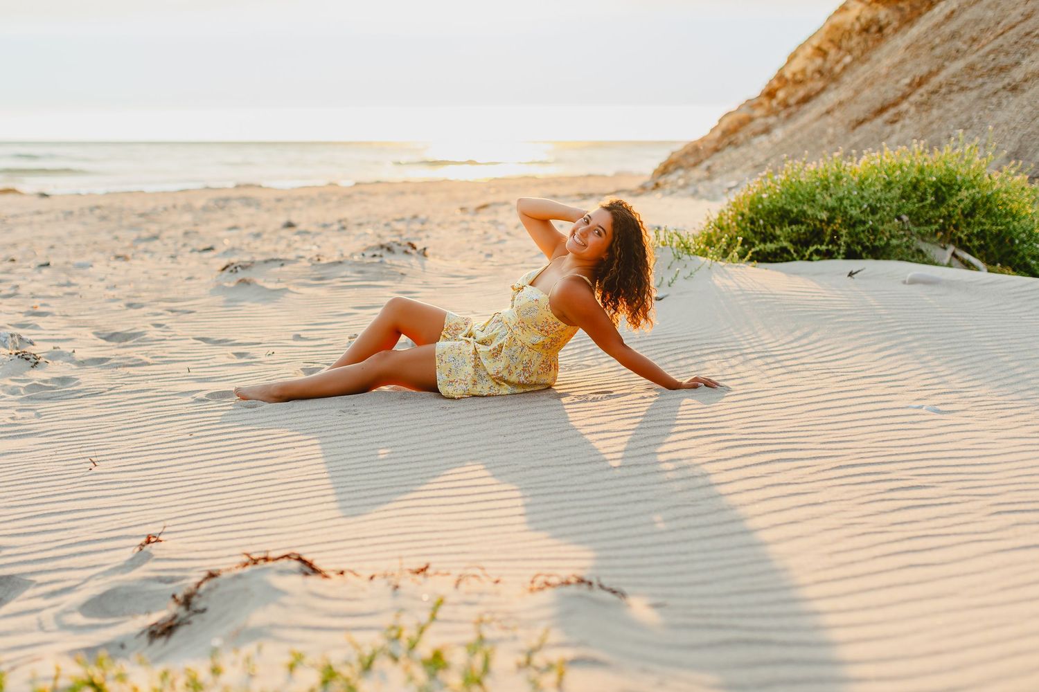 A person lounges on a sandy beach at sunset, creating long shadows across the rippled sand.
