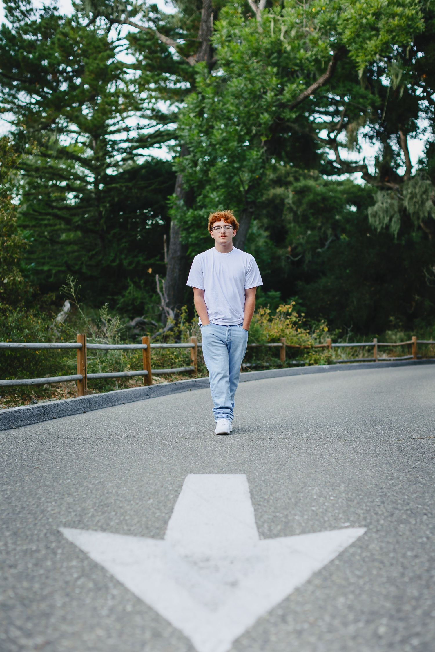Young redhead teen in white t-shirt and jeans walking on road with arrow marking in park.
