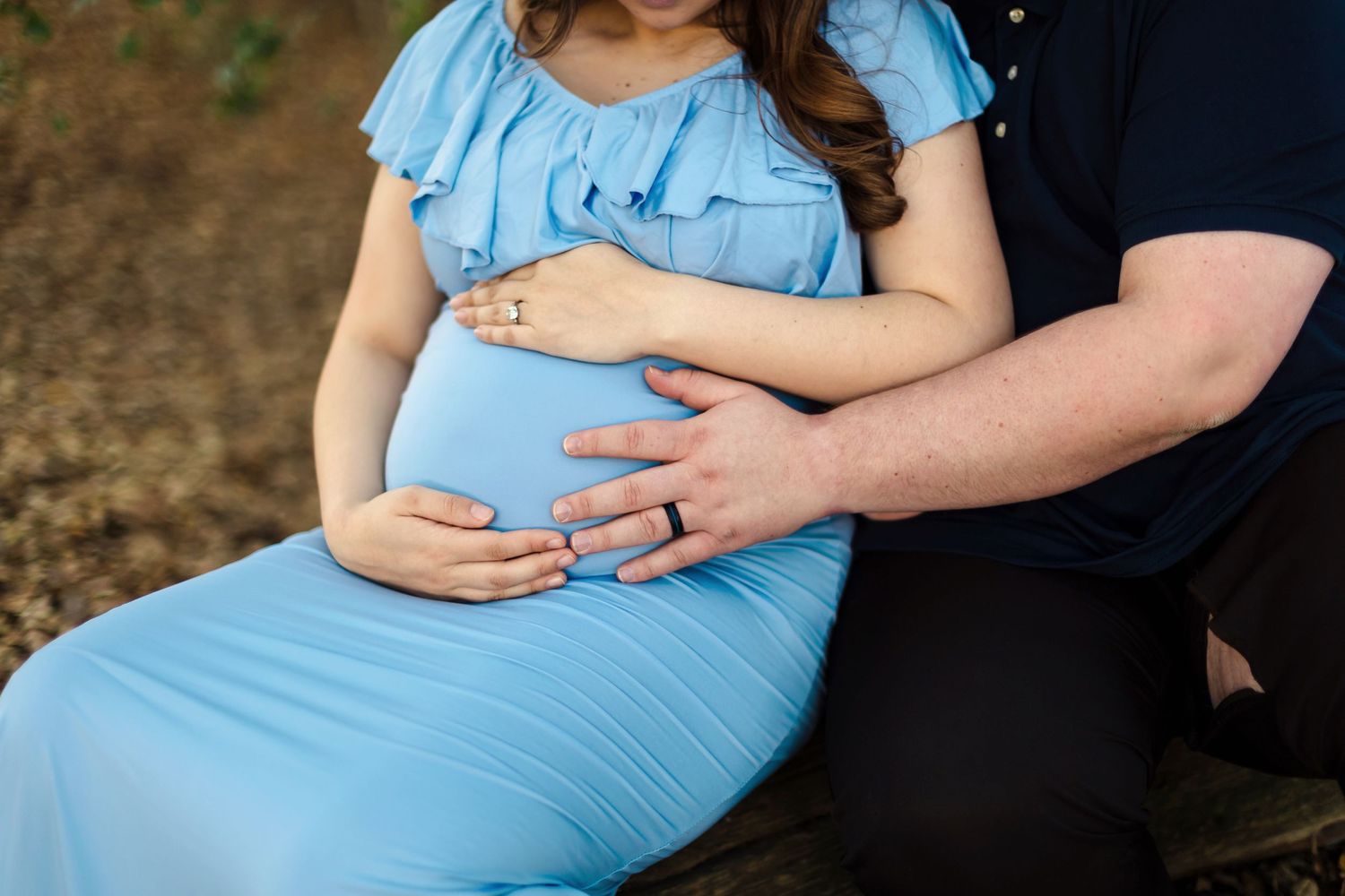 A pregnant couple embraces outdoors in coordinating blue and black outfits as they pose for maternity photos.