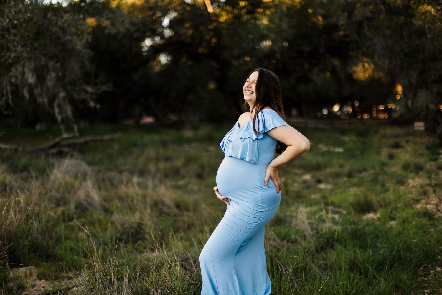 A person in a light blue dress poses outdoors in a series of nature-inspired maternity photos during golden hour.