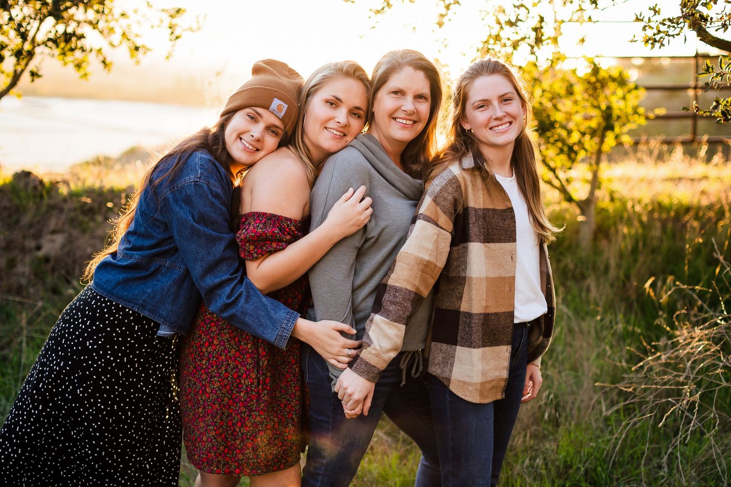 Group of people hugging and laughing together in a golden sunlit field during sunset.