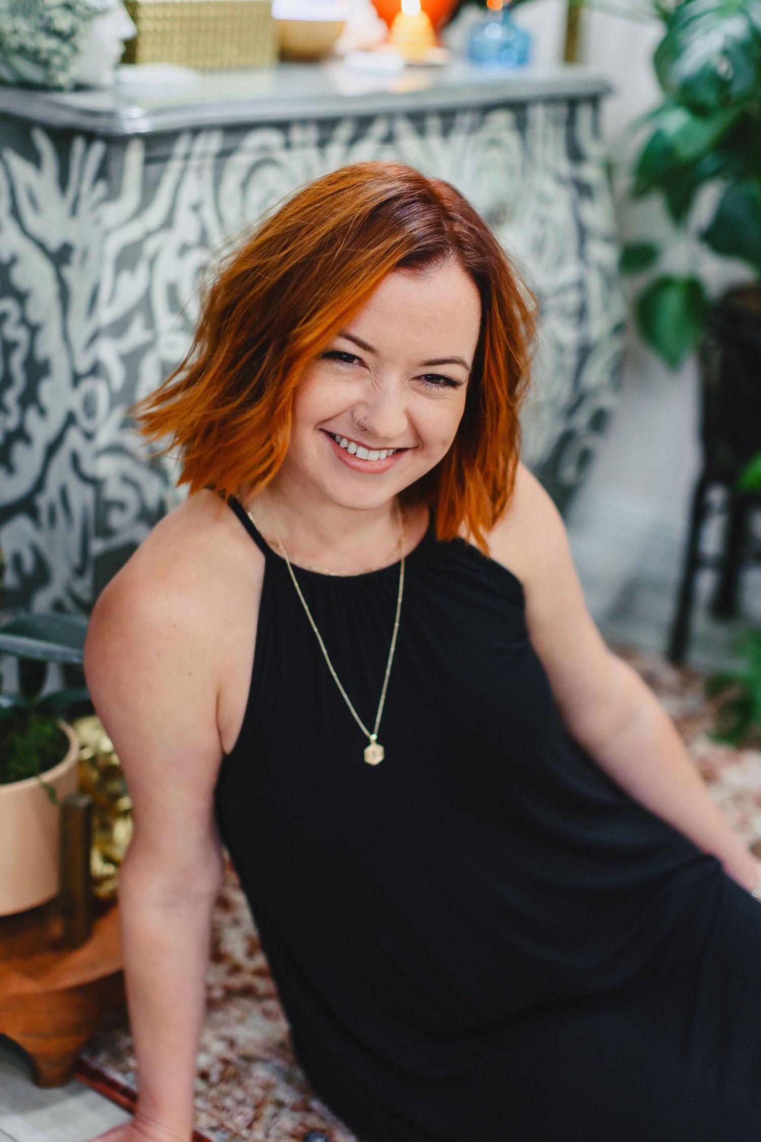 Casual portrait of person with orange hair sitting outdoors among decorative elements.