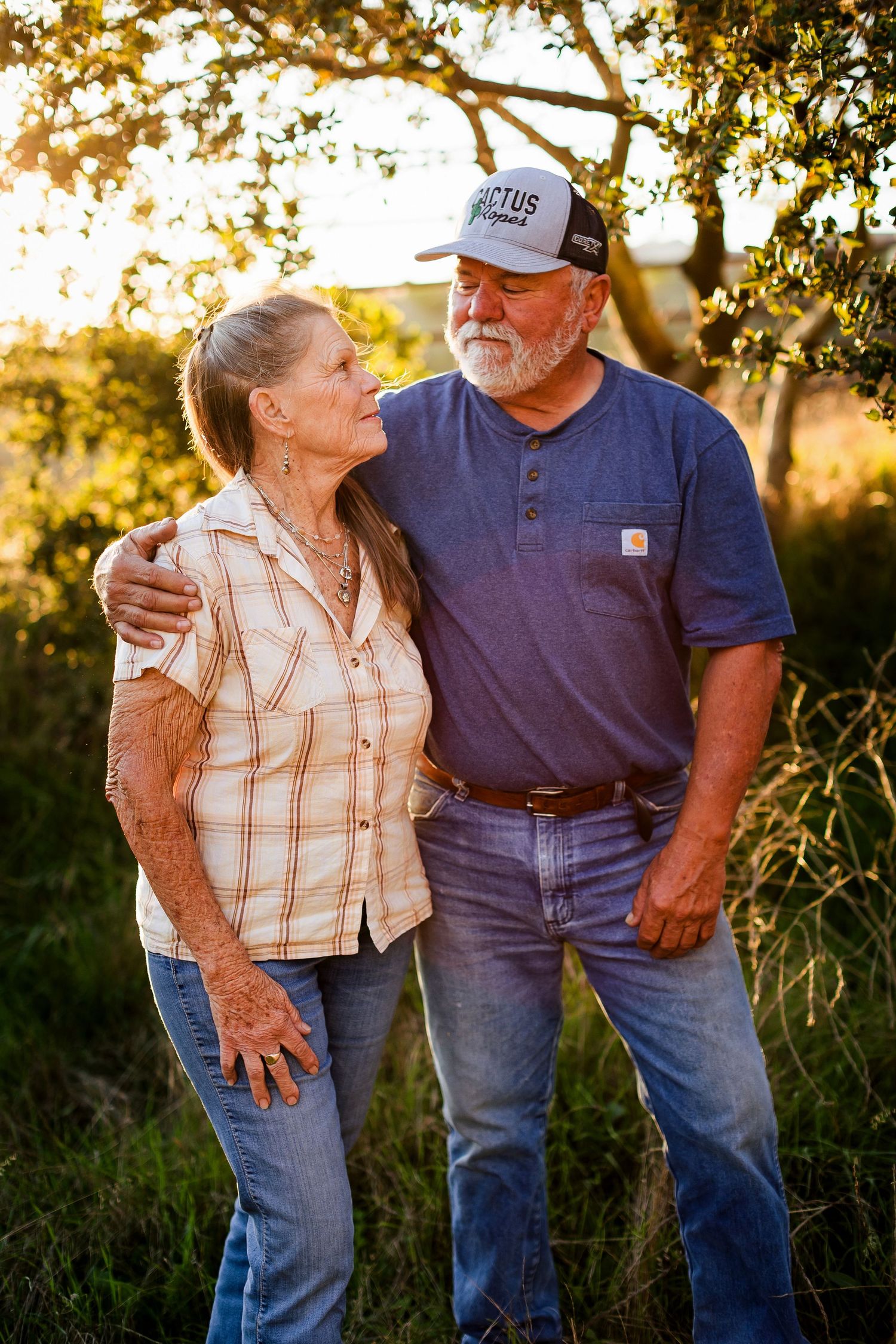 An elderly couple shares a tender moment in warm golden sunlight while wearing casual clothing.
