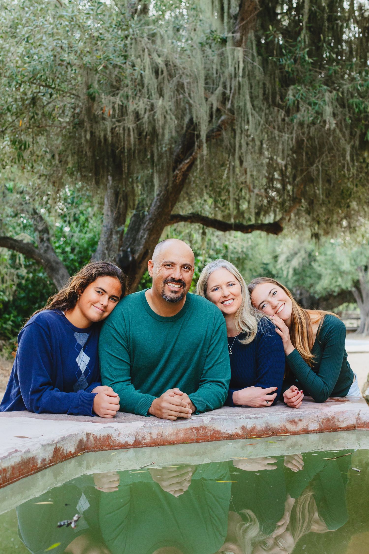 Family of four posing together by reflective pond with Spanish moss hanging from trees.