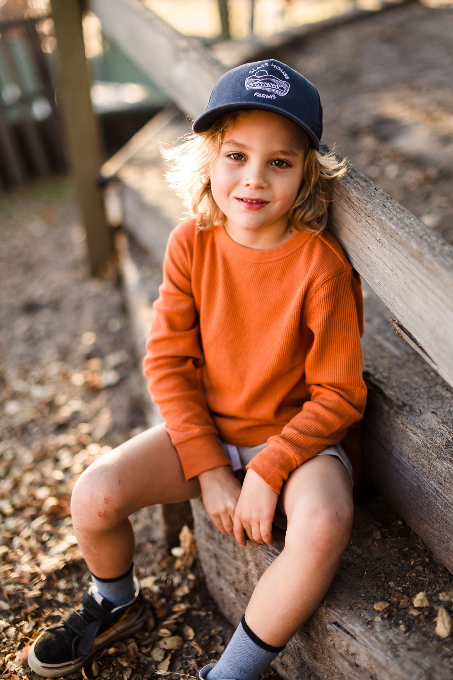 A series of candid moments showing a young child in a bright orange sweatshirt sitting on a wooden bench outdoors.