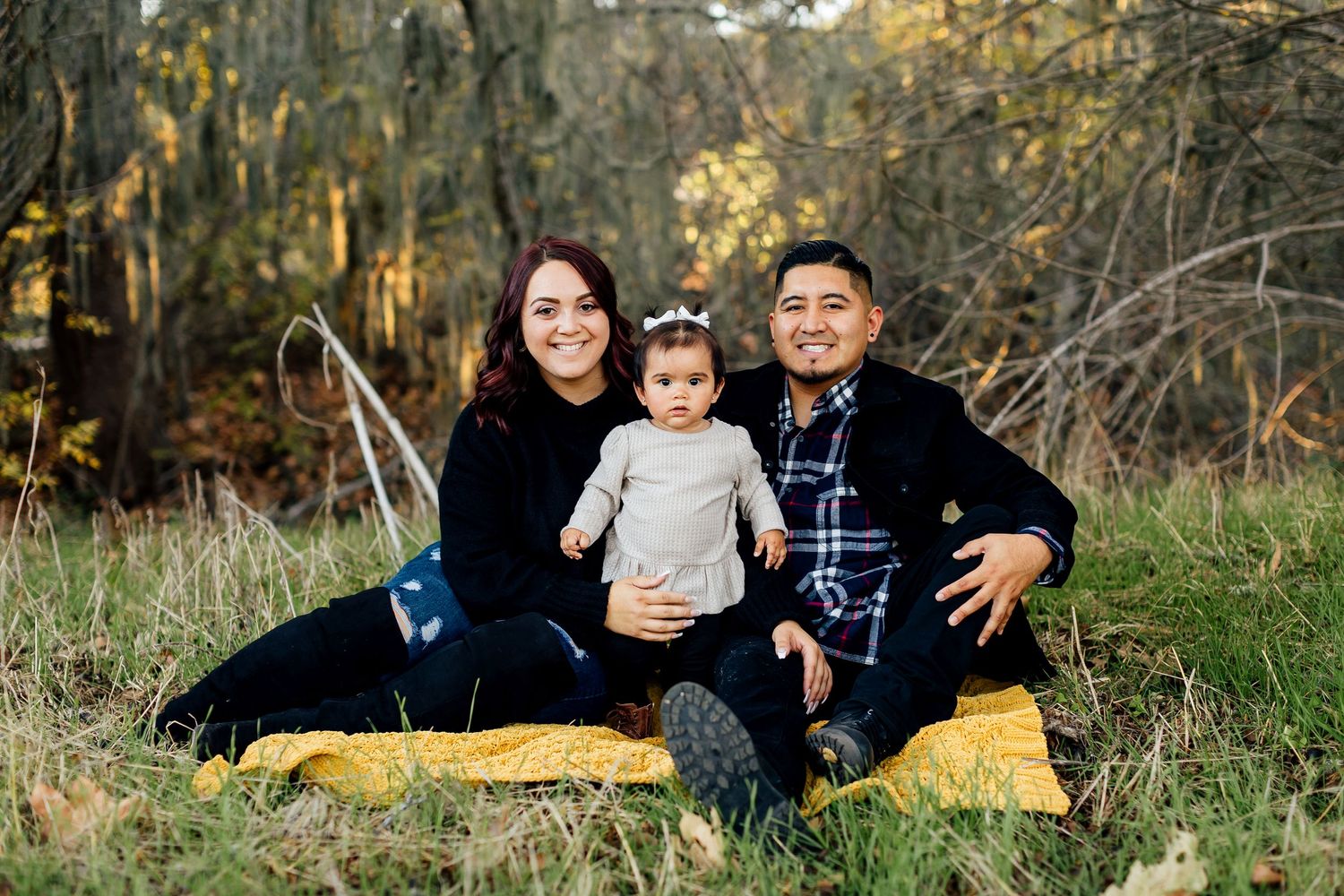 Three people sit together on a yellow blanket outdoors during a fall photo session in nature.