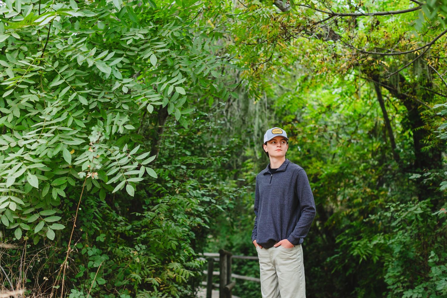 A person wearing a blue sweater stands on a path amidst lush green foliage in a wooded area.