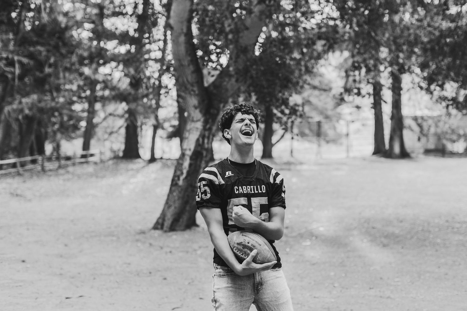 Black and white photo of a young football player in a Cariello jersey laughing outdoors near trees.