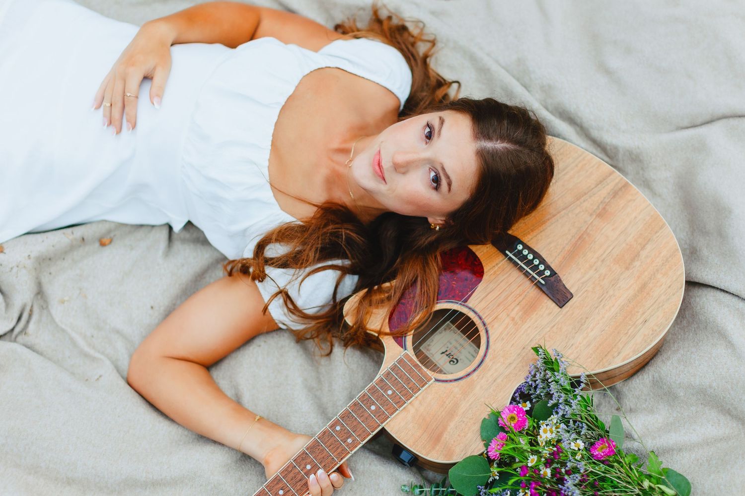 Young woman with curly hair lying on blanket beside acoustic guitar and wildflowers.